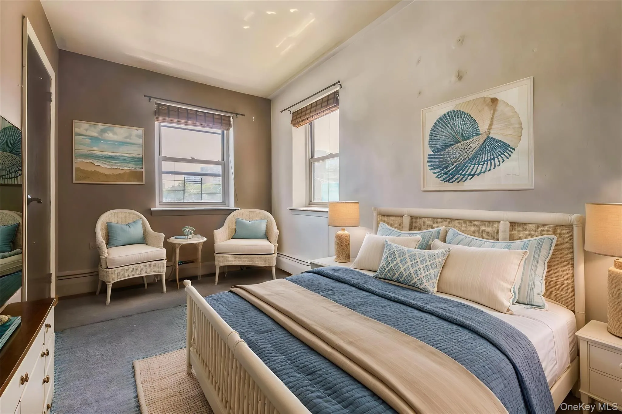 Bedroom featuring two large windows with blinds, a light-colored headboard with woven detailing, and soft blue carpeting Bedroom featuring two large windows with blinds, a light-colored headboard with woven detailing, and soft blue carpeting