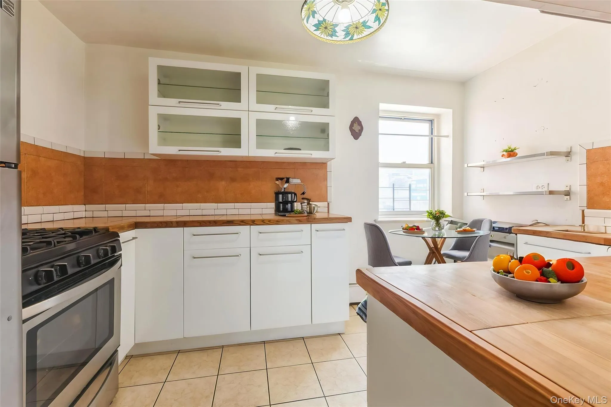 Kitchen featuring white cabinetry, light wood-finish countertops, stainless steel gas range, and tile flooring Kitchen featuring white cabinetry, light wood-finish countertops, stainless steel gas range, and tile flooring