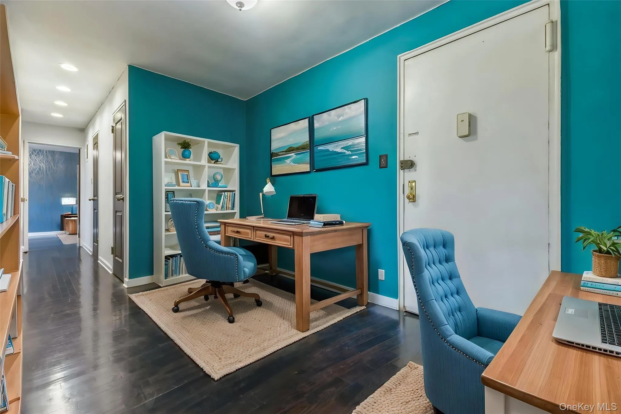 Dedicated workspace featuring vibrant accent wall, dark wood-finish flooring, recessed lighting, white built-in shelving, and solid core entry door Dedicated workspace featuring vibrant accent wall, dark wood-finish flooring, recessed lighting, white built-in shelving, and solid core entry door