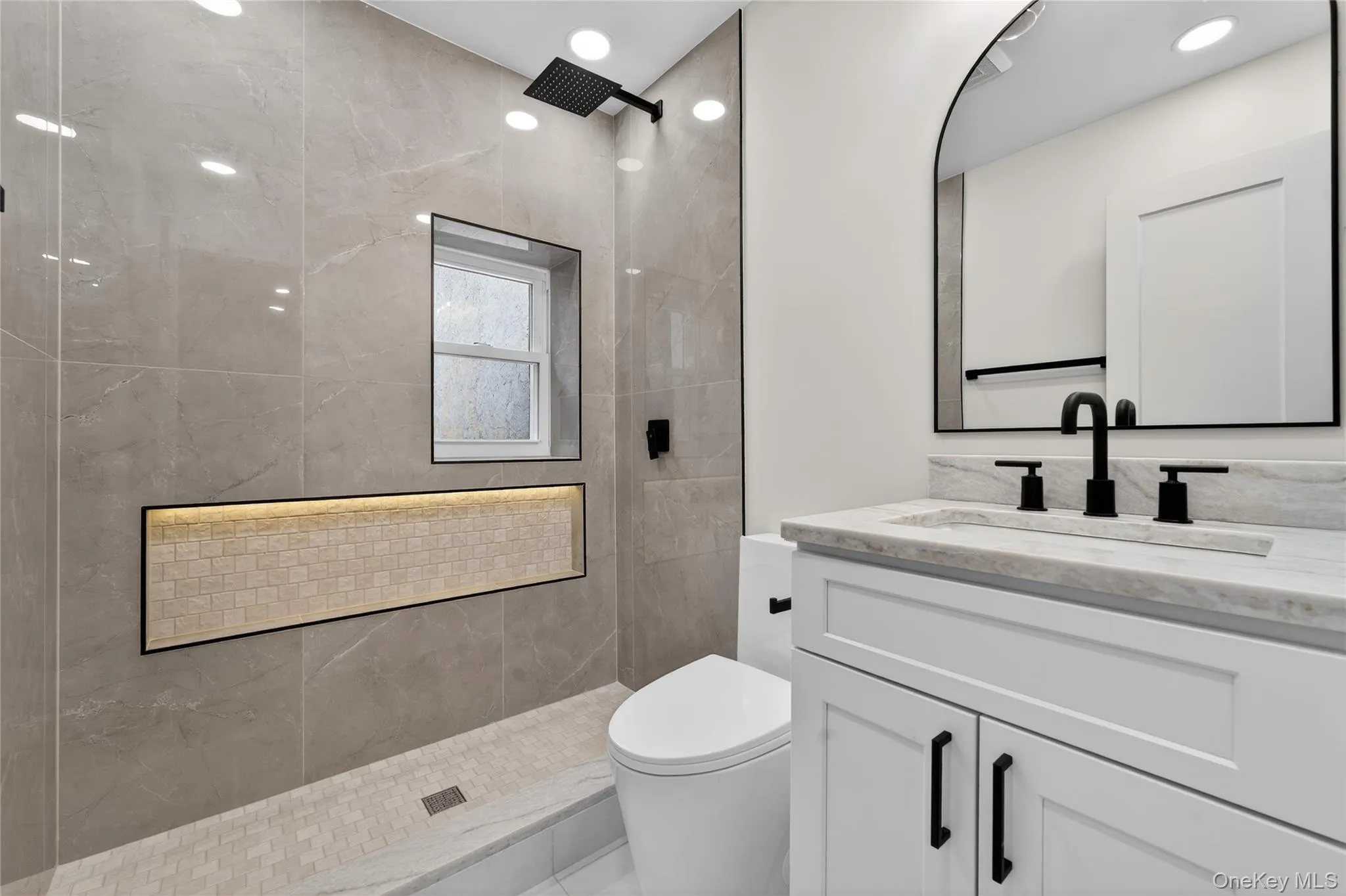 Bathroom featuring a walk-in shower with large-format tile, a window, and an illuminated mosaic-tiled niche Bathroom featuring a walk-in shower with large-format tile, a window, and an illuminated mosaic-tiled niche