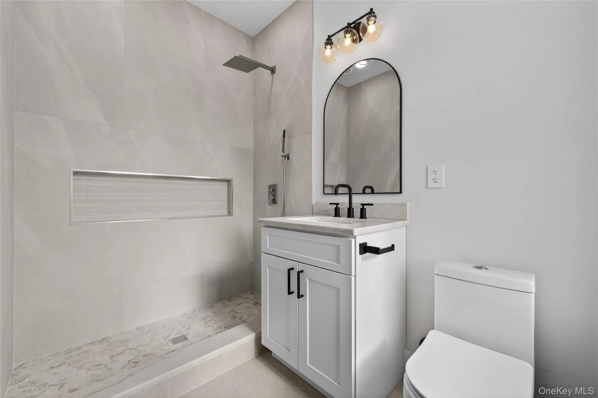 Bathroom featuring a walk-in shower with a rain shower head, built-in niche, and large format wall tiling Bathroom featuring a walk-in shower with a rain shower head, built-in niche, and large format wall tiling