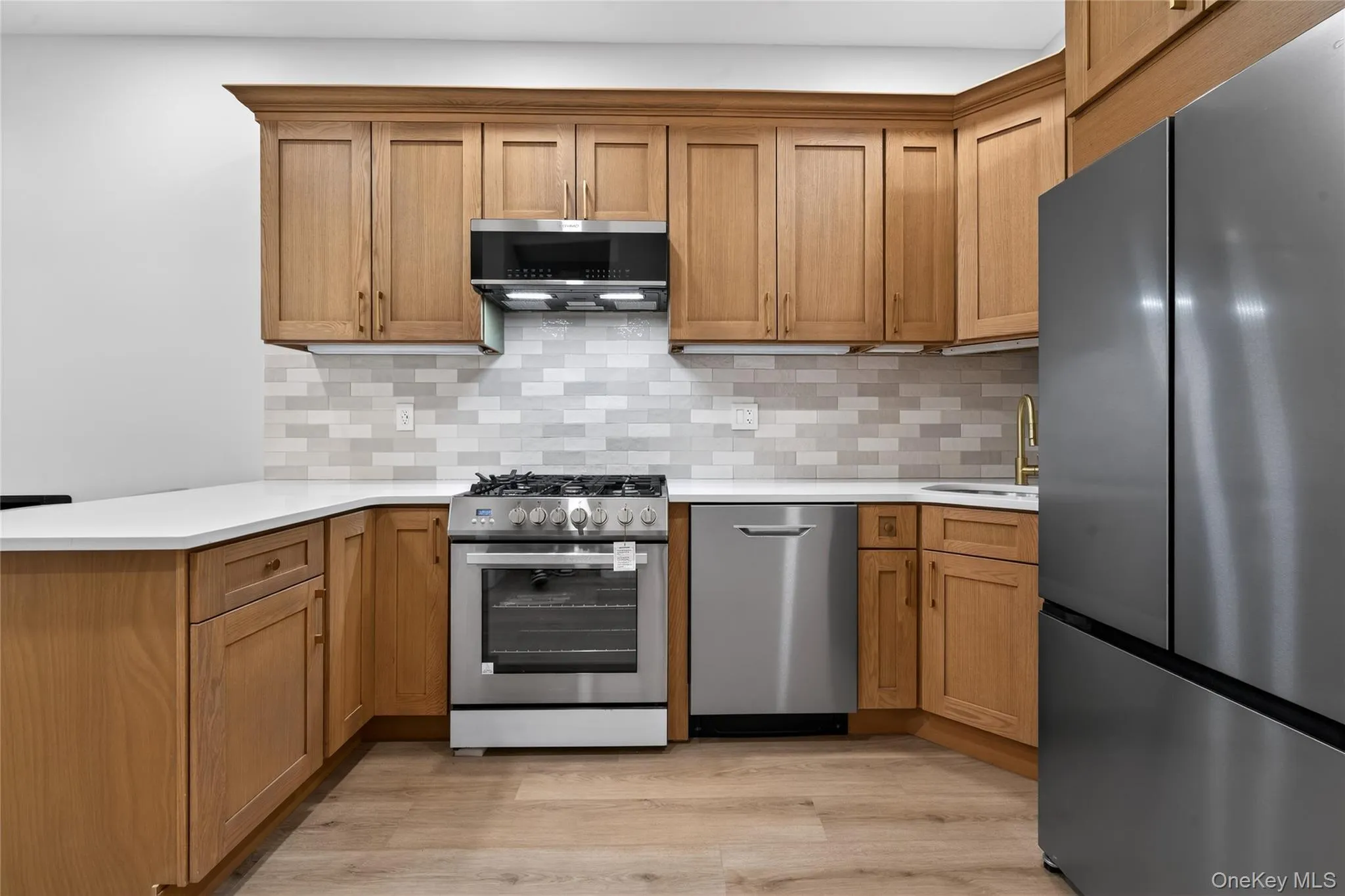 Modern kitchen featuring wood-finish cabinetry, white countertops, and a subway tile backsplash Modern kitchen featuring wood-finish cabinetry, white countertops, and a subway tile backsplash