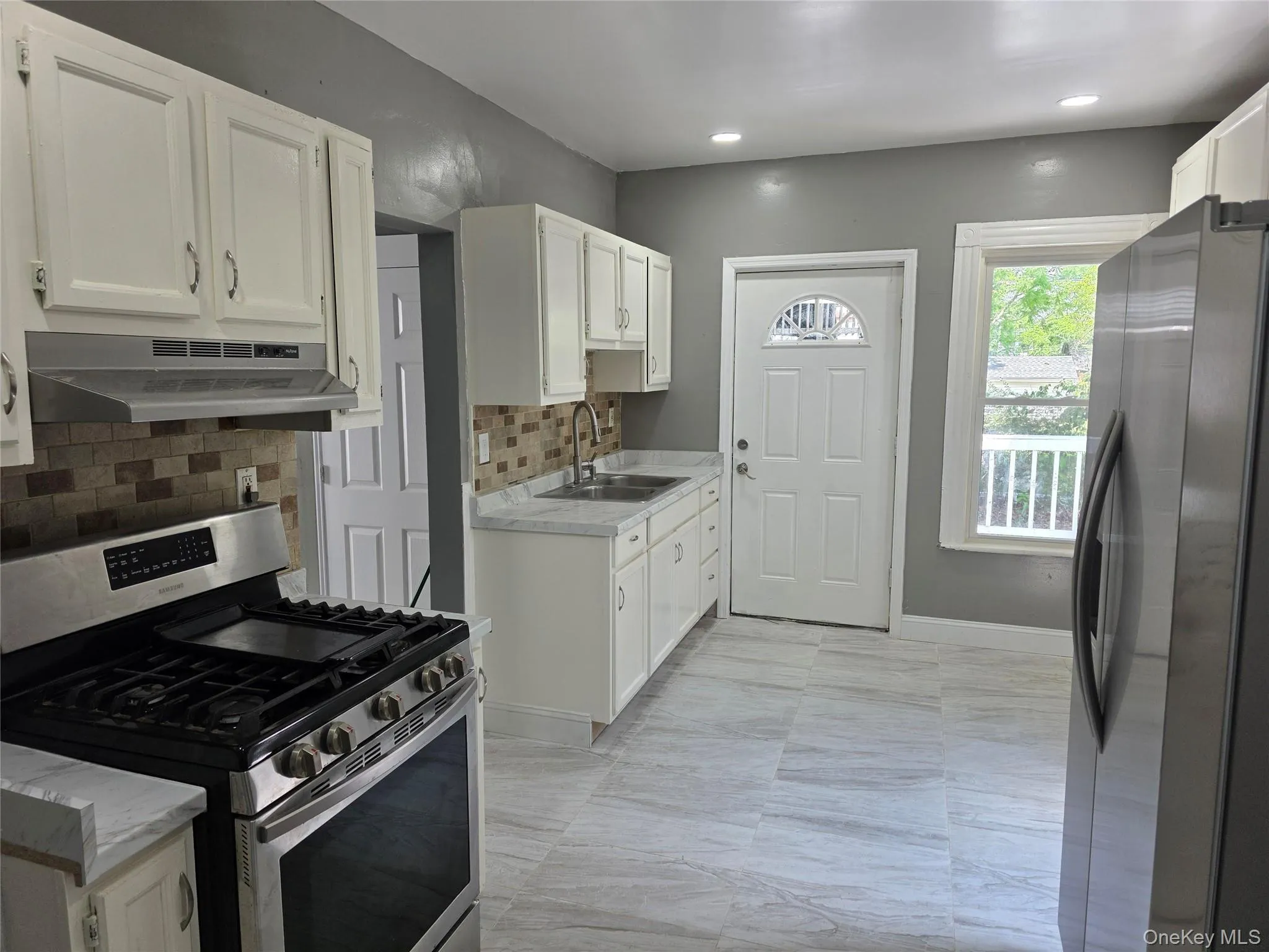Kitchen featuring white cabinetry, stainless steel appliances, a tile backsplash, light-toned countertops, and wood-finish flooring Kitchen featuring white cabinetry, stainless steel appliances, a tile backsplash, light-toned countertops, and wood-finish flooring
