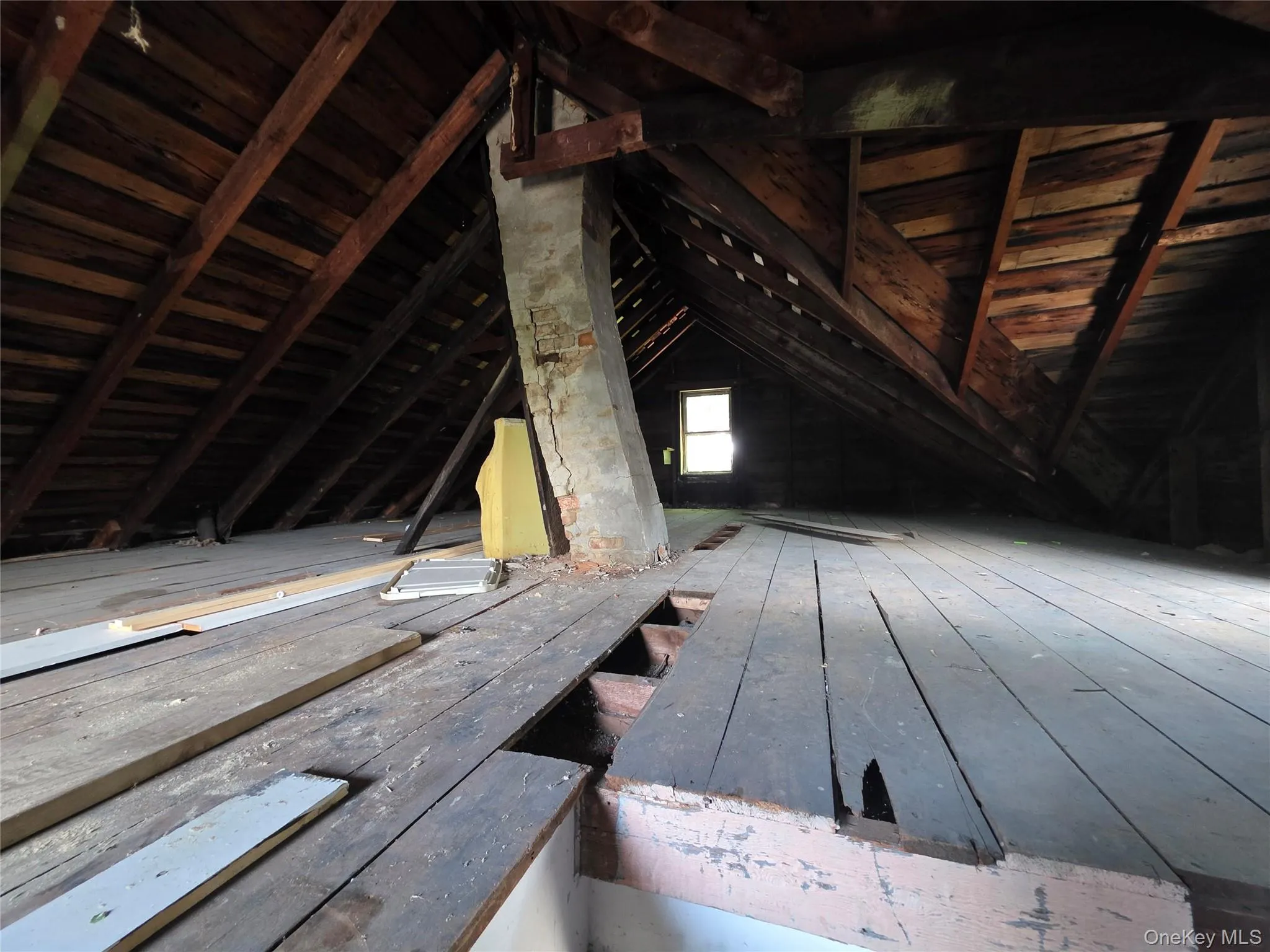 Expansive attic space featuring exposed wood rafters, wood plank flooring, and a visible brick chimney structure Expansive attic space featuring exposed wood rafters, wood plank flooring, and a visible brick chimney structure
