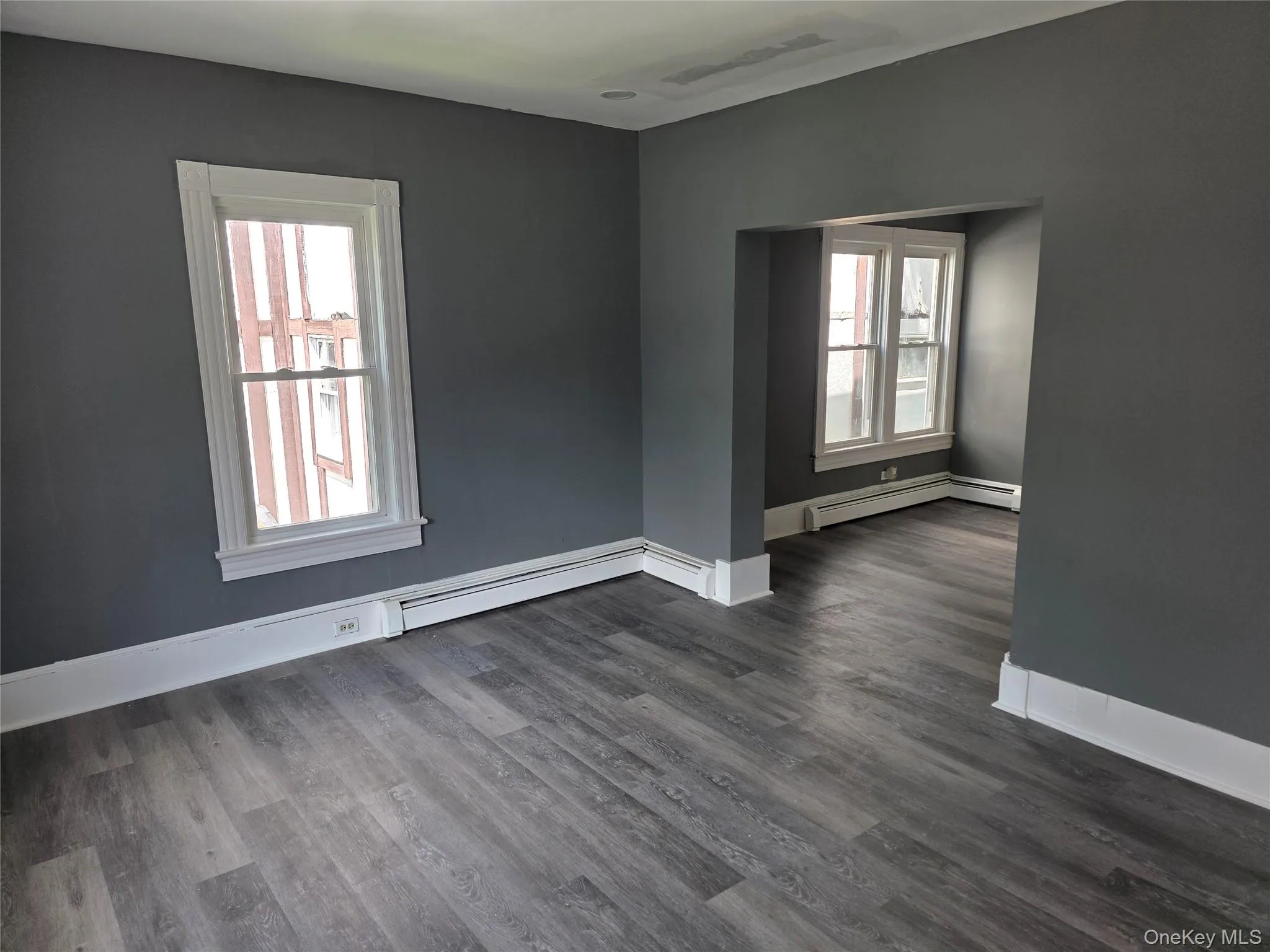 Spacious interior room with wood-finish flooring, neutral gray wall paint, and white trim molding Spacious interior room with wood-finish flooring, neutral gray wall paint, and white trim molding