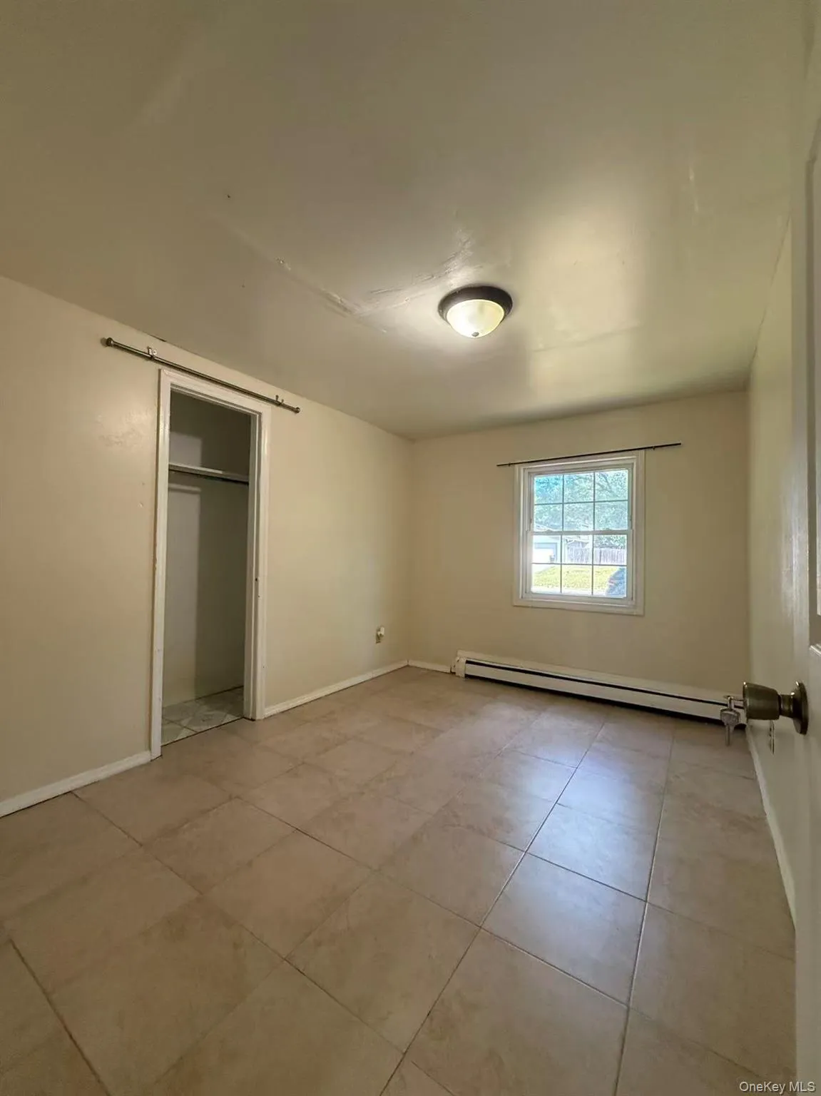 Room featuring neutral-toned tile flooring, a window providing natural light, and a built-in wall-mounted heater Room featuring neutral-toned tile flooring, a window providing natural light, and a built-in wall-mounted heater