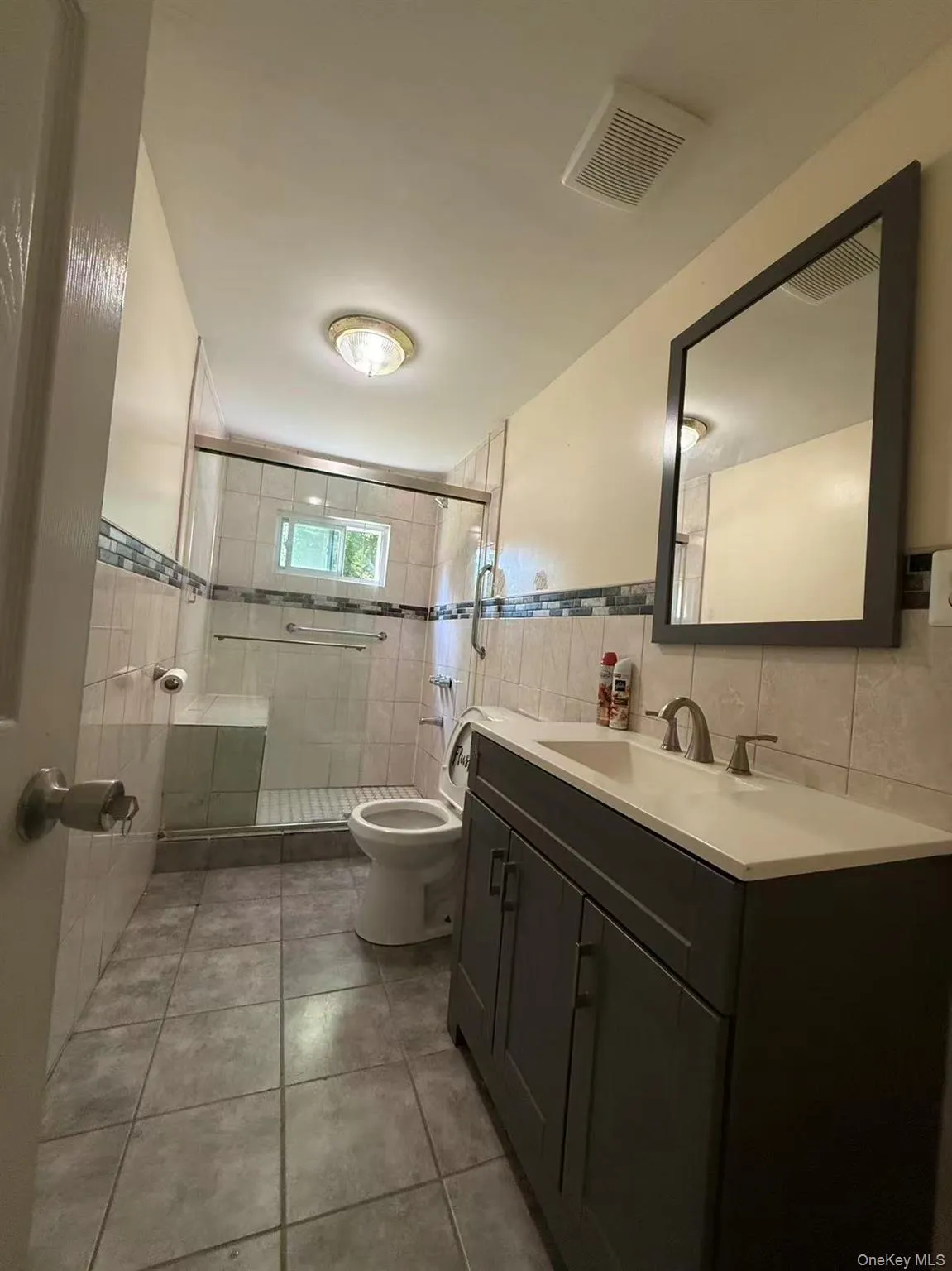 Bathroom featuring a dark gray vanity with a white countertop, an integrated rectangular sink, and a framed mirror Bathroom featuring a dark gray vanity with a white countertop, an integrated rectangular sink, and a framed mirror