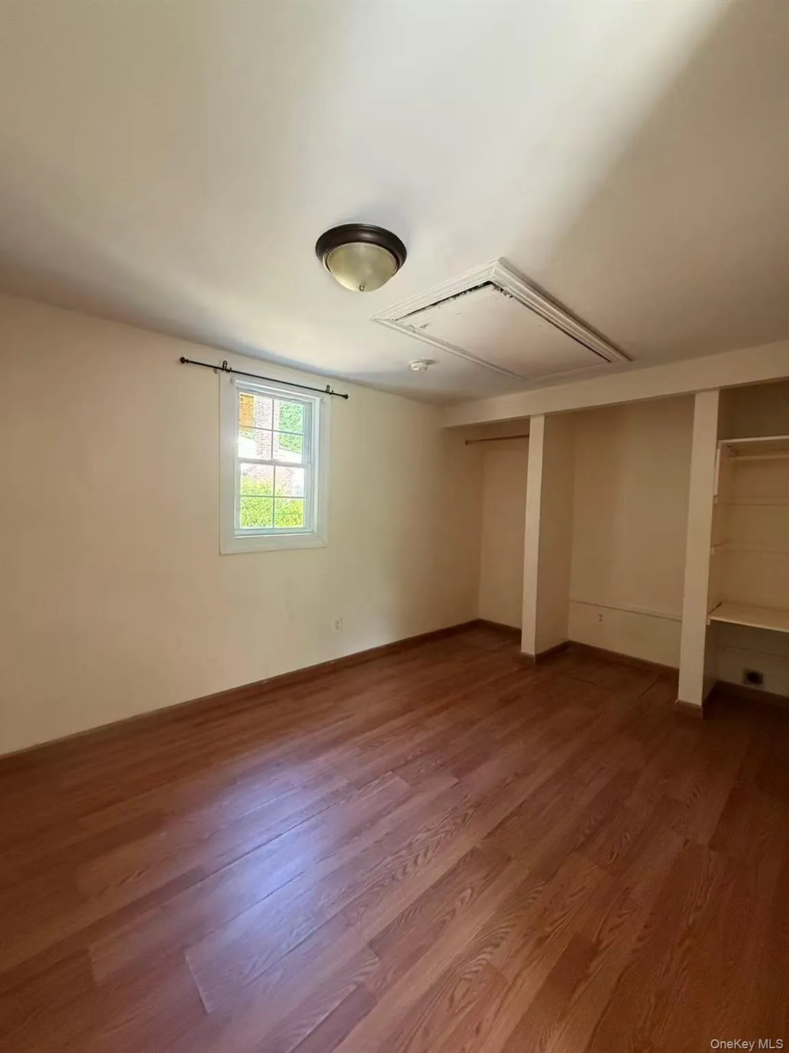 Bright room featuring wood-finish flooring, a double-hung window, and built-in closet shelving Bright room featuring wood-finish flooring, a double-hung window, and built-in closet shelving