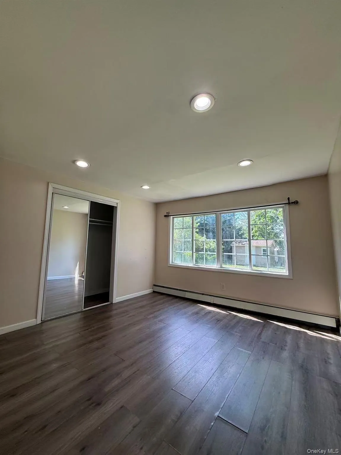 Spacious room featuring wood-finish flooring, recessed lighting, a large window, and mirrored closet doors Spacious room featuring wood-finish flooring, recessed lighting, a large window, and mirrored closet doors