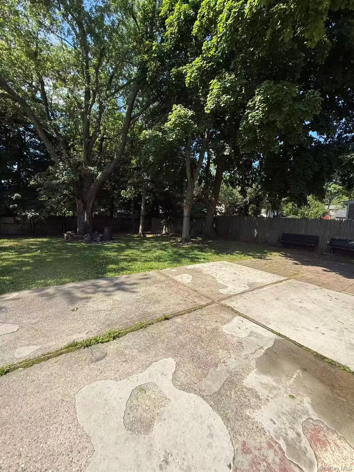 Expansive backyard featuring a large concrete patio, a brick pathway, mature trees, and two storage sheds Expansive backyard featuring a large concrete patio, a brick pathway, mature trees, and two storage sheds