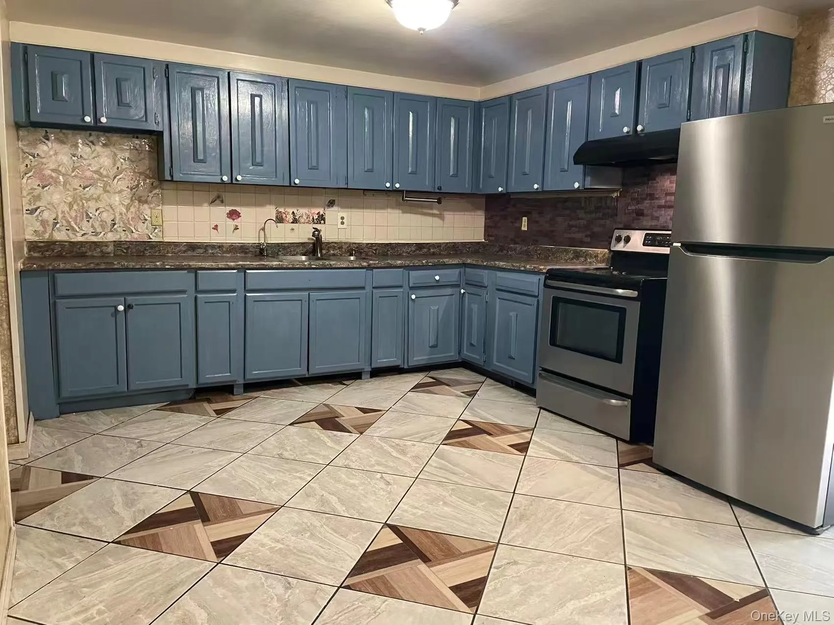 Kitchen featuring blue cabinetry, dark countertops, a stainless steel refrigerator, and a stainless steel range with overhead ventilation Kitchen featuring blue cabinetry, dark countertops, a stainless steel refrigerator, and a stainless steel range with overhead ventilation