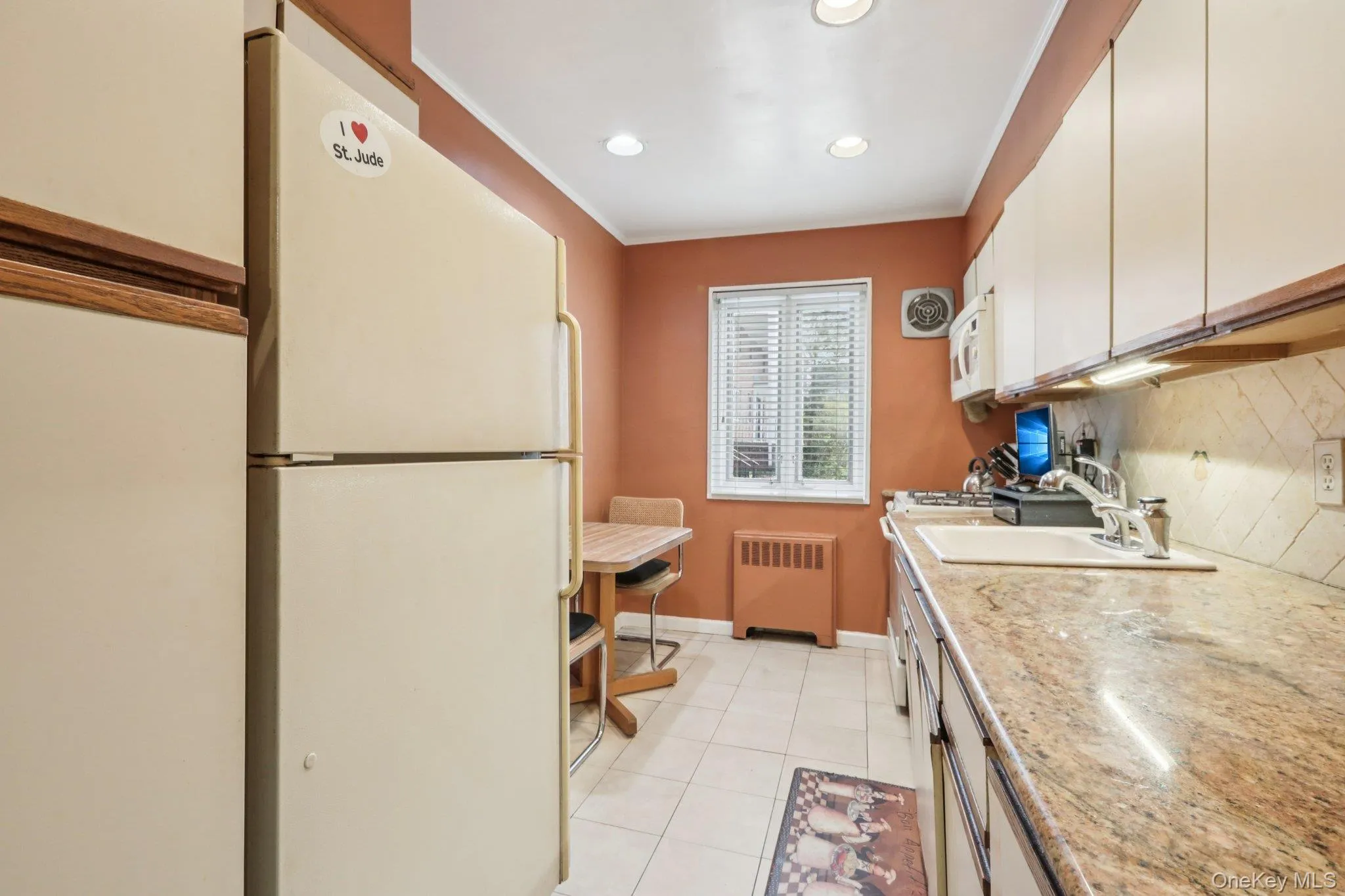 Kitchen featuring white appliances, light tile patterned flooring, radiator heating unit, crown molding, and recessed lighting Kitchen featuring white appliances, light tile patterned flooring, radiator heating unit, crown molding, and recessed lighting