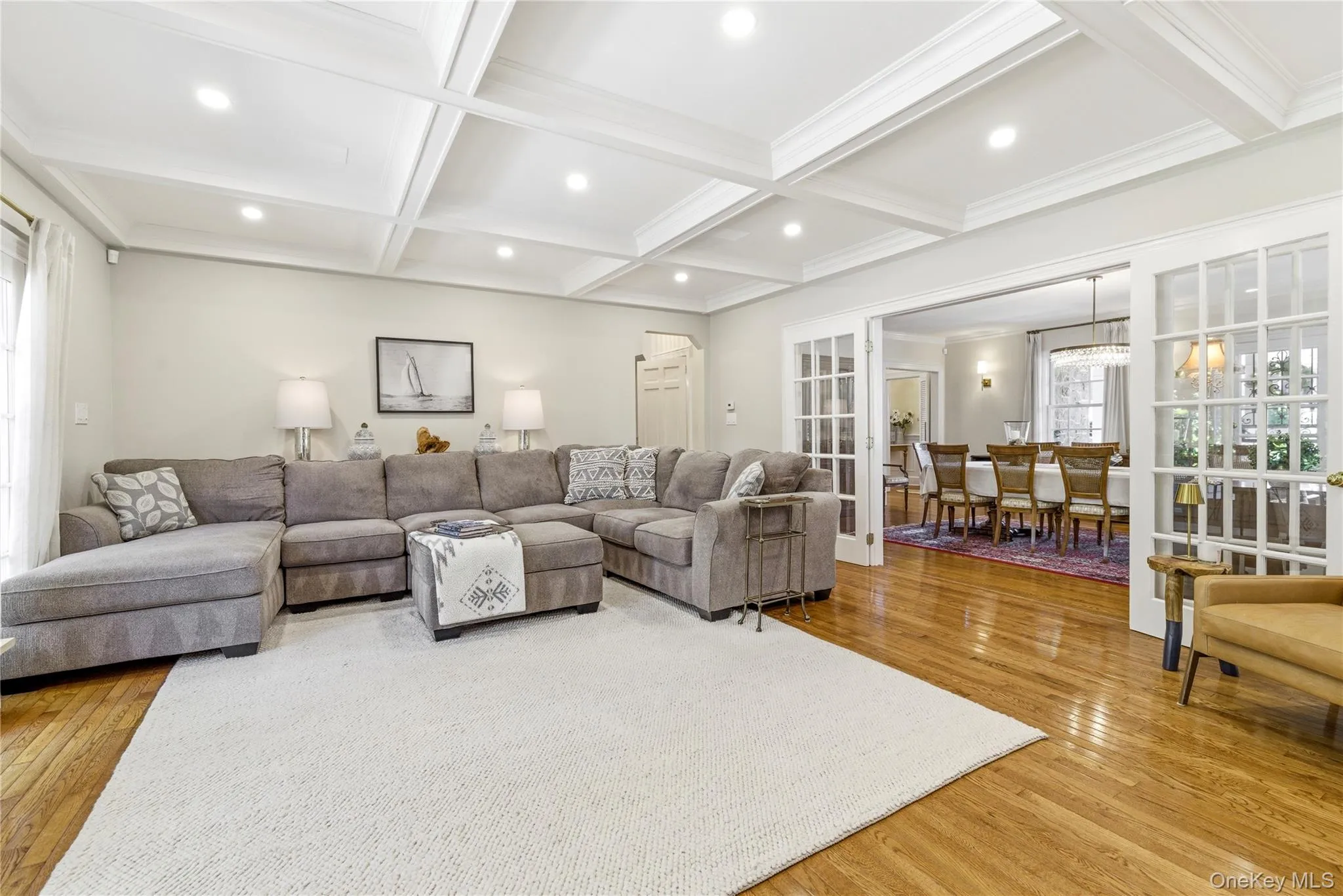 Living area featuring wood-finish flooring, a coffered ceiling with recessed lighting, and French doors opening to a dining room Living area featuring wood-finish flooring, a coffered ceiling with recessed lighting, and French doors opening to a dining room