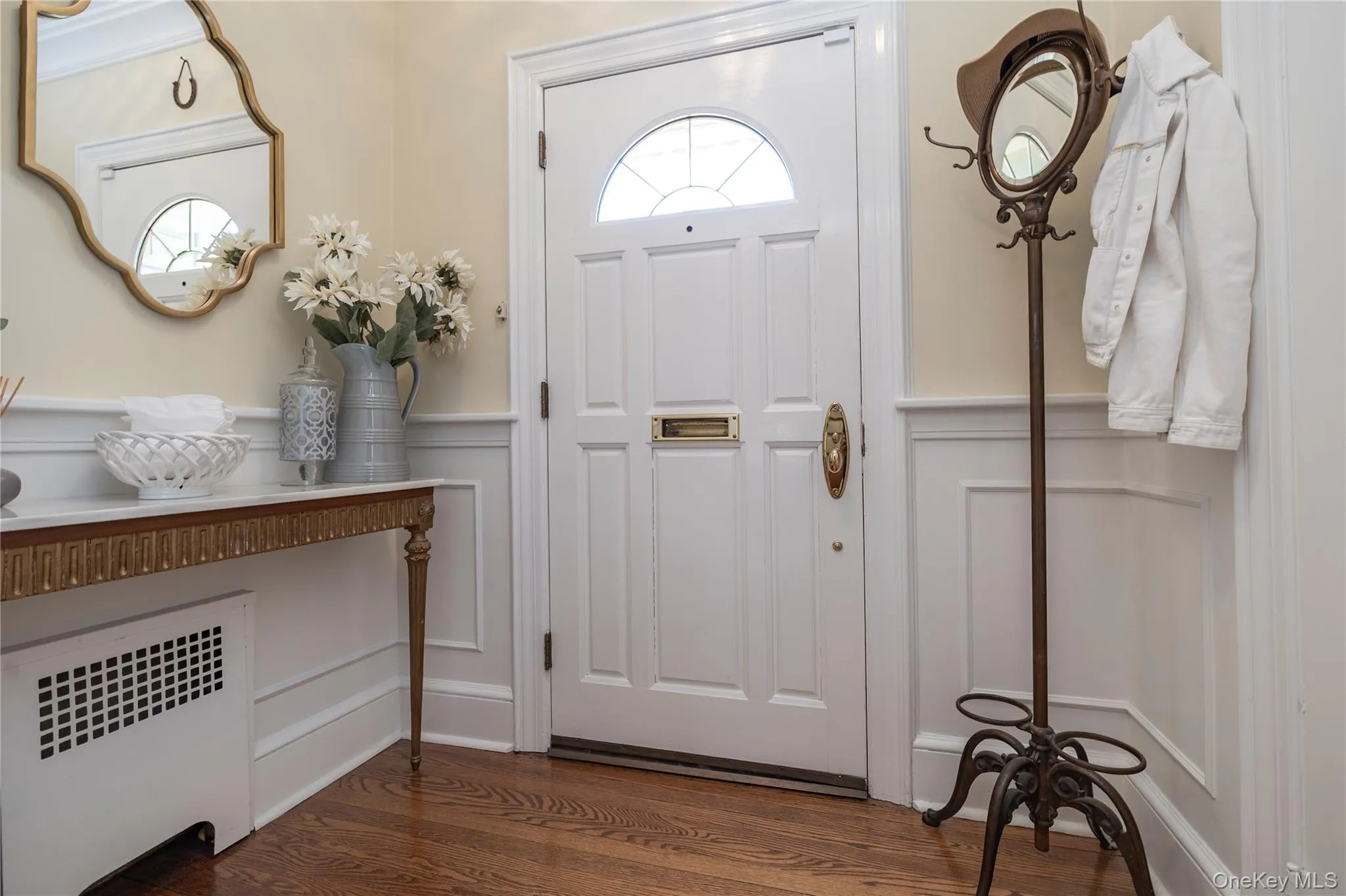 Entryway featuring a paneled door with an arched glass insert, brass hardware, and wood-finish flooring Entryway featuring a paneled door with an arched glass insert, brass hardware, and wood-finish flooring