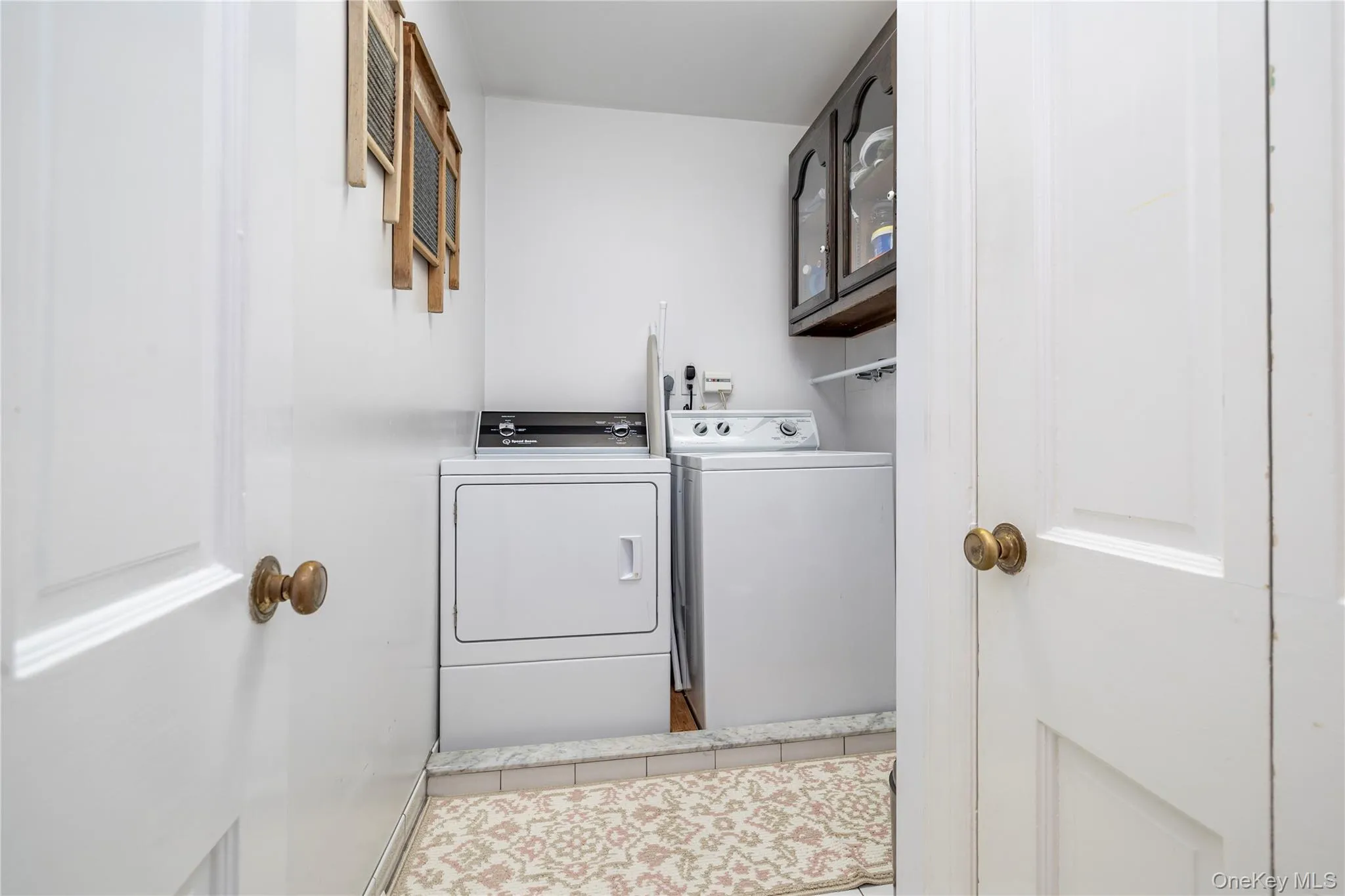 Dedicated 2nd floor laundry area featuring a white dryer and washer, an overhead wood-finish cabinet with glass inserts, and a white wall shelf Dedicated 2nd floor laundry area featuring a white dryer and washer, an overhead wood-finish cabinet with glass inserts, and a white wall shelf