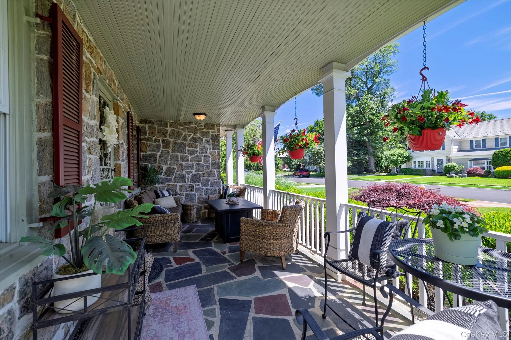 Expansive covered front porch featuring a stone facade, multi-color flagstone flooring, white pillars, and a beadboard ceiling with recessed lighting Expansive covered front porch featuring a stone facade, multi-color flagstone flooring, white pillars, and a beadboard ceiling with recessed lighting