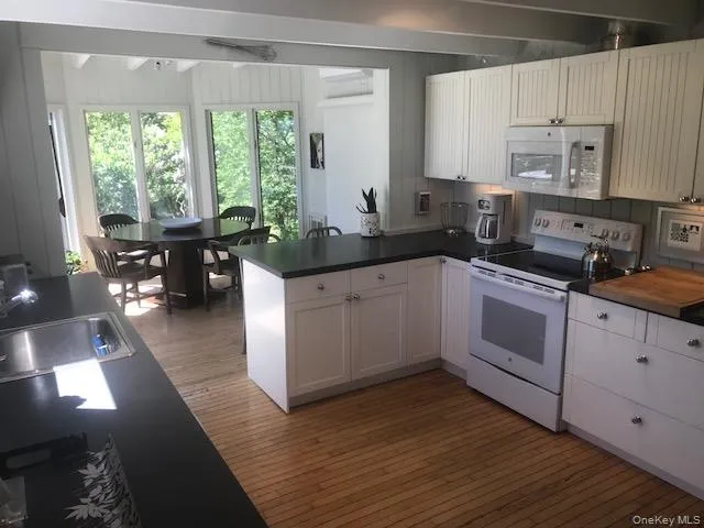 Kitchen with white appliances, a peninsula, light wood-type flooring, a sink, and dark countertops Kitchen with white appliances, a peninsula, light wood-type flooring, a sink, and dark countertops