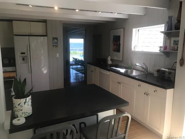 Kitchen with white refrigerator with ice dispenser, a sink, dishwasher, dark countertops, and beamed ceiling Kitchen with white refrigerator with ice dispenser, a sink, dishwasher, dark countertops, and beamed ceiling
