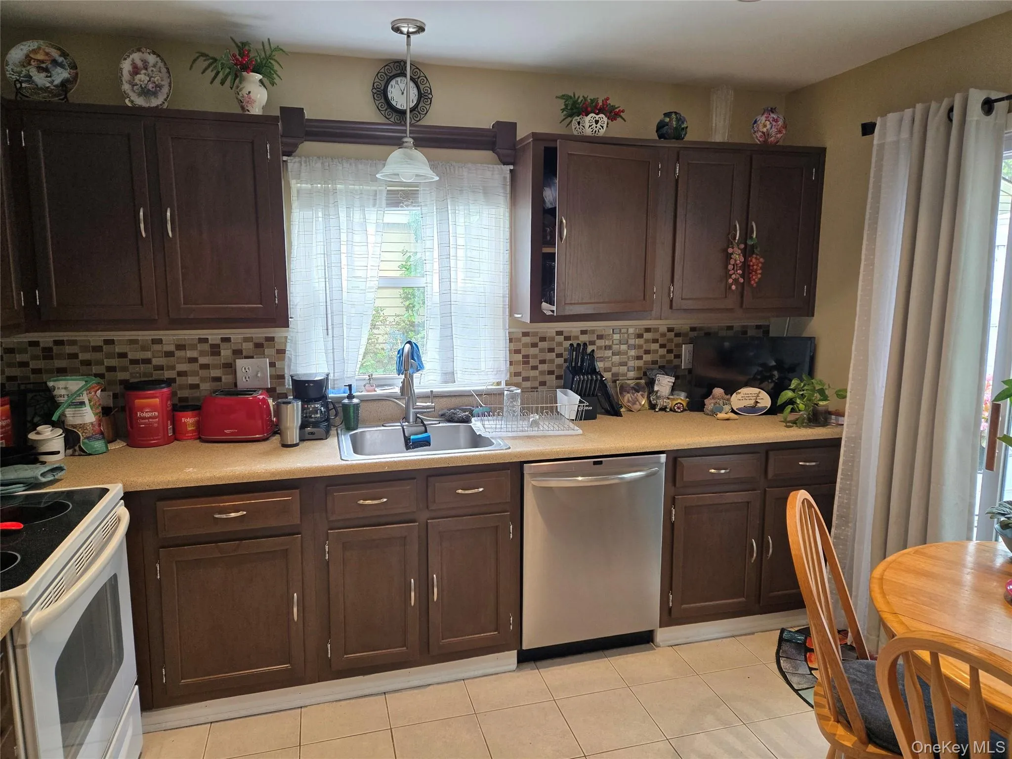Kitchen featuring dark wood-finish cabinetry, a mosaic tile backsplash, and a stainless steel dishwasher with sliding doors leading to patio Kitchen featuring dark wood-finish cabinetry, a mosaic tile backsplash, and a stainless steel dishwasher with sliding doors leading to patio