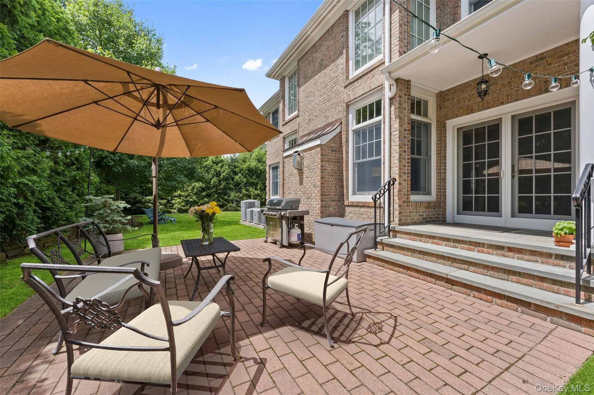 Expansive brick paver patio featuring a manicured lawn and mature privacy landscaping Expansive brick paver patio featuring a manicured lawn and mature privacy landscaping