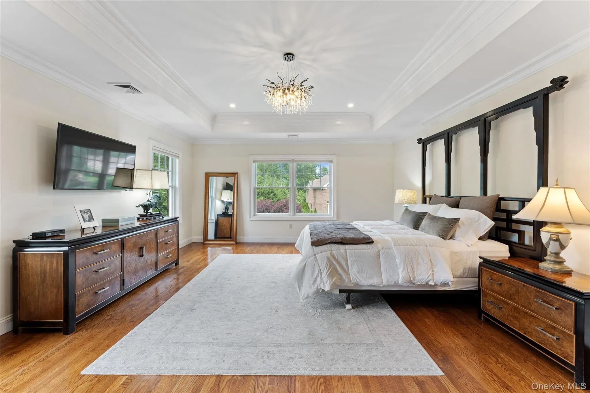 Primary Bedroom with hardwood flooring throughout featuring a tray ceiling with recessed lighting and a central chandelier Primary Bedroom with hardwood flooring throughout featuring a tray ceiling with recessed lighting and a central chandelier