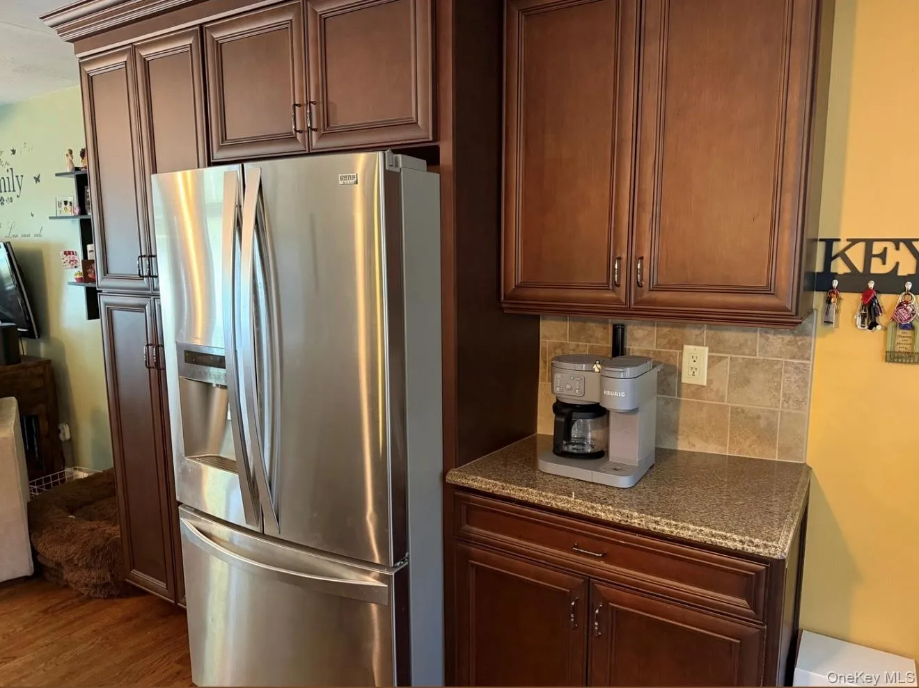 Kitchen featuring wood-finish cabinetry with crown molding, stainless steel refrigerator, tile backsplash, and speckled countertop. Digitally removed personal items Kitchen featuring wood-finish cabinetry with crown molding, stainless steel refrigerator, tile backsplash, and speckled countertop. Digitally removed personal items