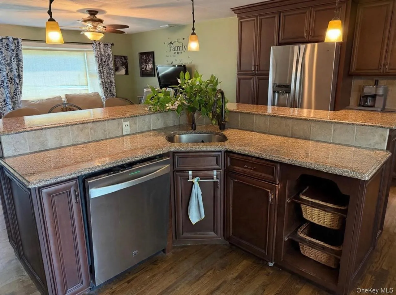 Kitchen island featuring a stainless steel sink with a high-arch faucet, granite countertops, an integrated dishwasher, and rich wood-finish cabinetry. Digitally removed personal items Kitchen island featuring a stainless steel sink with a high-arch faucet, granite countertops, an integrated dishwasher, and rich wood-finish cabinetry. Digitally removed personal items