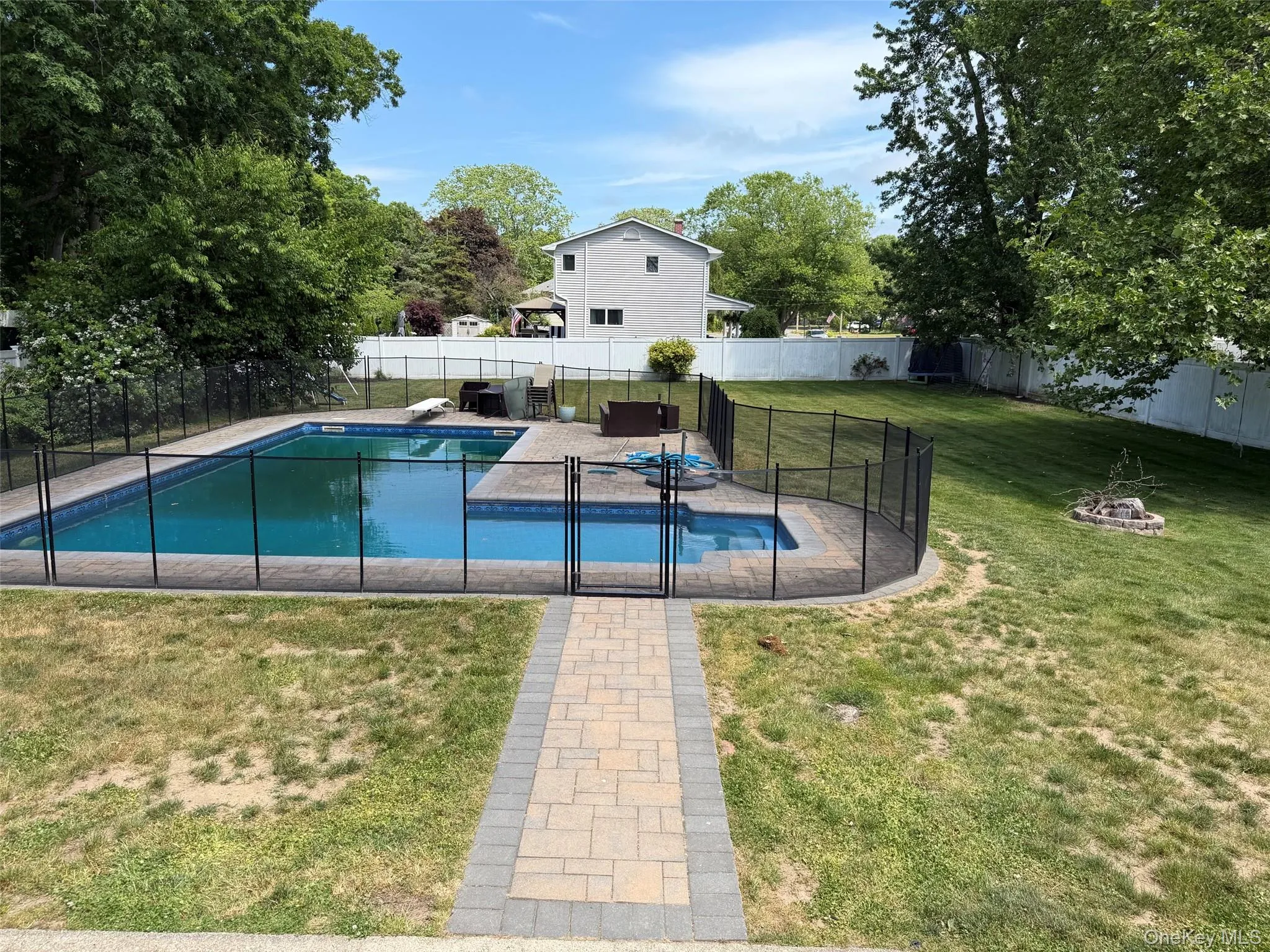 Fenced inground swimming pool featuring a paver patio surround, a separate wading area, and a stone fire pit area Fenced inground swimming pool featuring a paver patio surround, a separate wading area, and a stone fire pit area