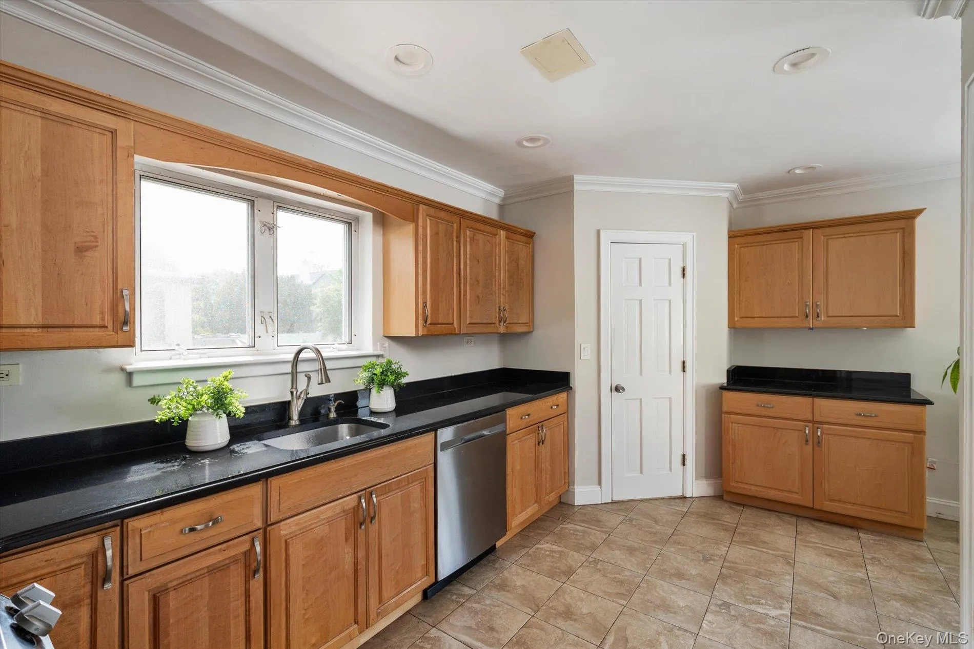 Kitchen featuring wood cabinetry, black countertops, stainless steel sink, stainless steel dishwasher, and tiled flooring Kitchen featuring wood cabinetry, black countertops, stainless steel sink, stainless steel dishwasher, and tiled flooring