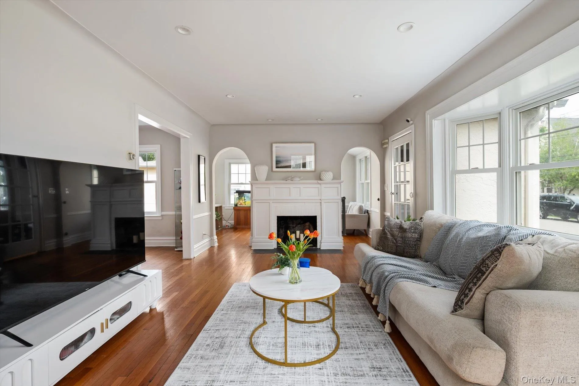 Spacious living area featuring rich wood-finish flooring, a decorative fireplace with an ornate mantel, and recessed lighting Spacious living area featuring rich wood-finish flooring, a decorative fireplace with an ornate mantel, and recessed lighting