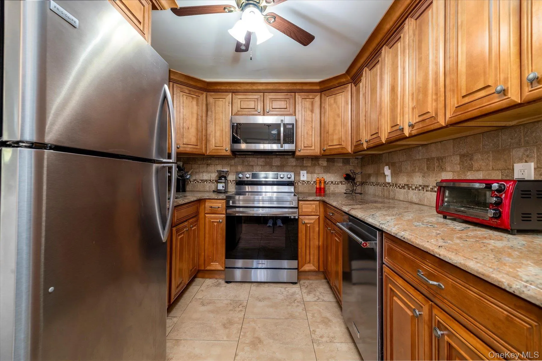 Kitchen featuring stainless steel appliances, wood cabinetry, stone countertops, and tile flooring Kitchen featuring stainless steel appliances, wood cabinetry, stone countertops, and tile flooring