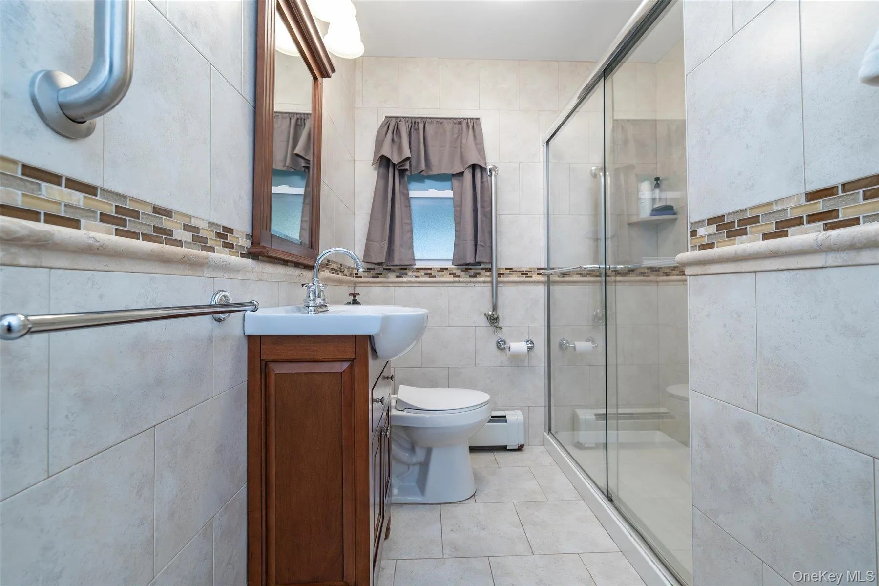 Bathroom featuring a glass-enclosed shower, a wall-mounted sink with a wood-finish vanity, and floor-to-ceiling tile Bathroom featuring a glass-enclosed shower, a wall-mounted sink with a wood-finish vanity, and floor-to-ceiling tile