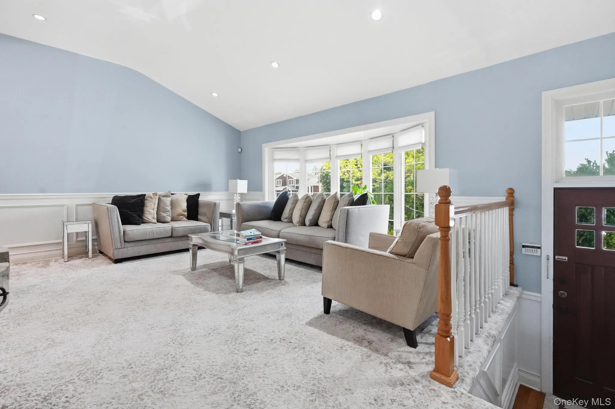Living space featuring a vaulted ceiling with recessed lighting, light blue walls, and white wainscoting Living space featuring a vaulted ceiling with recessed lighting, light blue walls, and white wainscoting
