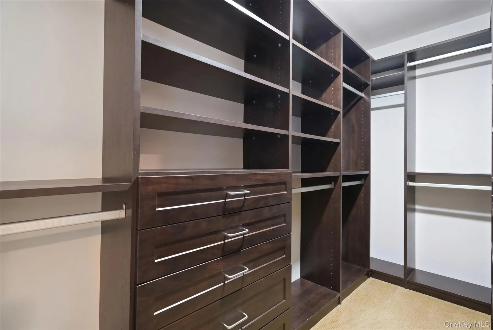 Custom closet system featuring dark wood-finish cabinetry, extensive shelving, integrated drawers with linear hardware, and multiple hanging rods Custom closet system featuring dark wood-finish cabinetry, extensive shelving, integrated drawers with linear hardware, and multiple hanging rods