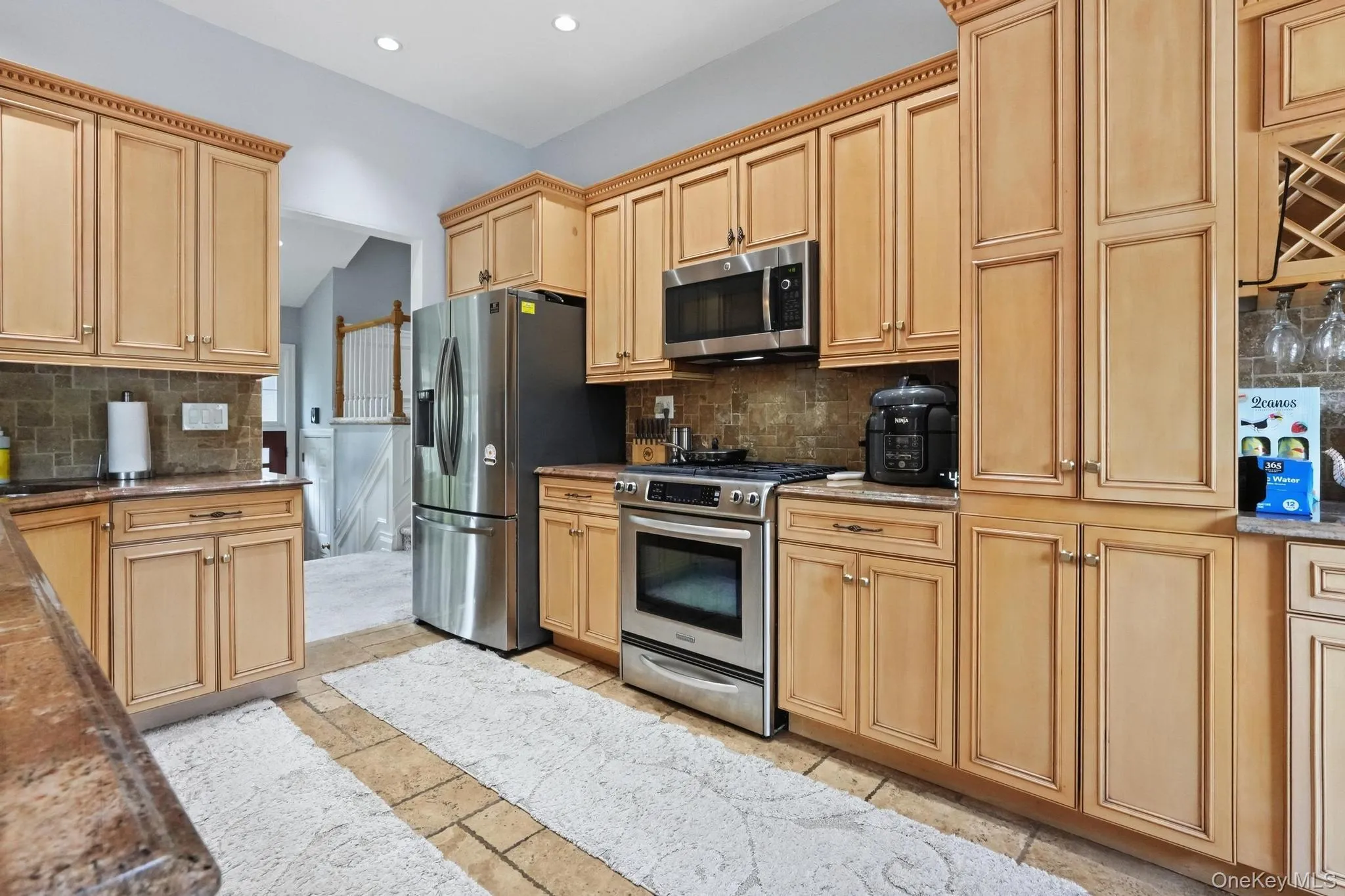 Kitchen featuring light wood cabinetry with crown molding, stainless steel appliances, stone tile flooring, and a tiled backsplash Kitchen featuring light wood cabinetry with crown molding, stainless steel appliances, stone tile flooring, and a tiled backsplash