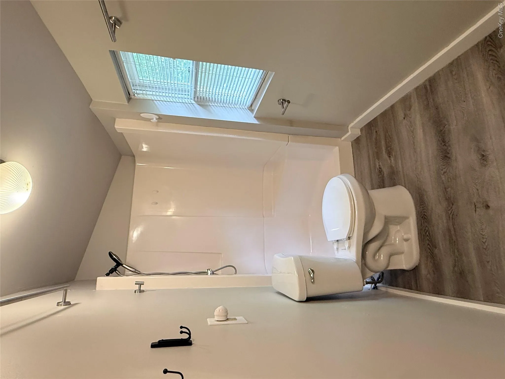 Bathroom with wood-finish flooring, a white toilet, and a white shower stall with a chrome showerhead Bathroom with wood-finish flooring, a white toilet, and a white shower stall with a chrome showerhead