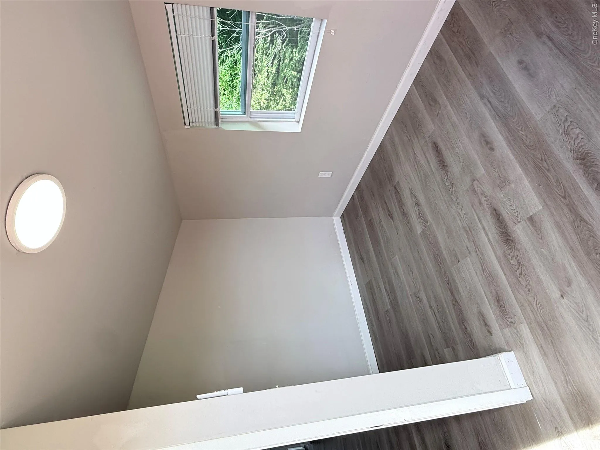 Light gray wood-finish flooring with white baseboards, neutral painted walls, and a single window with blinds Light gray wood-finish flooring with white baseboards, neutral painted walls, and a single window with blinds