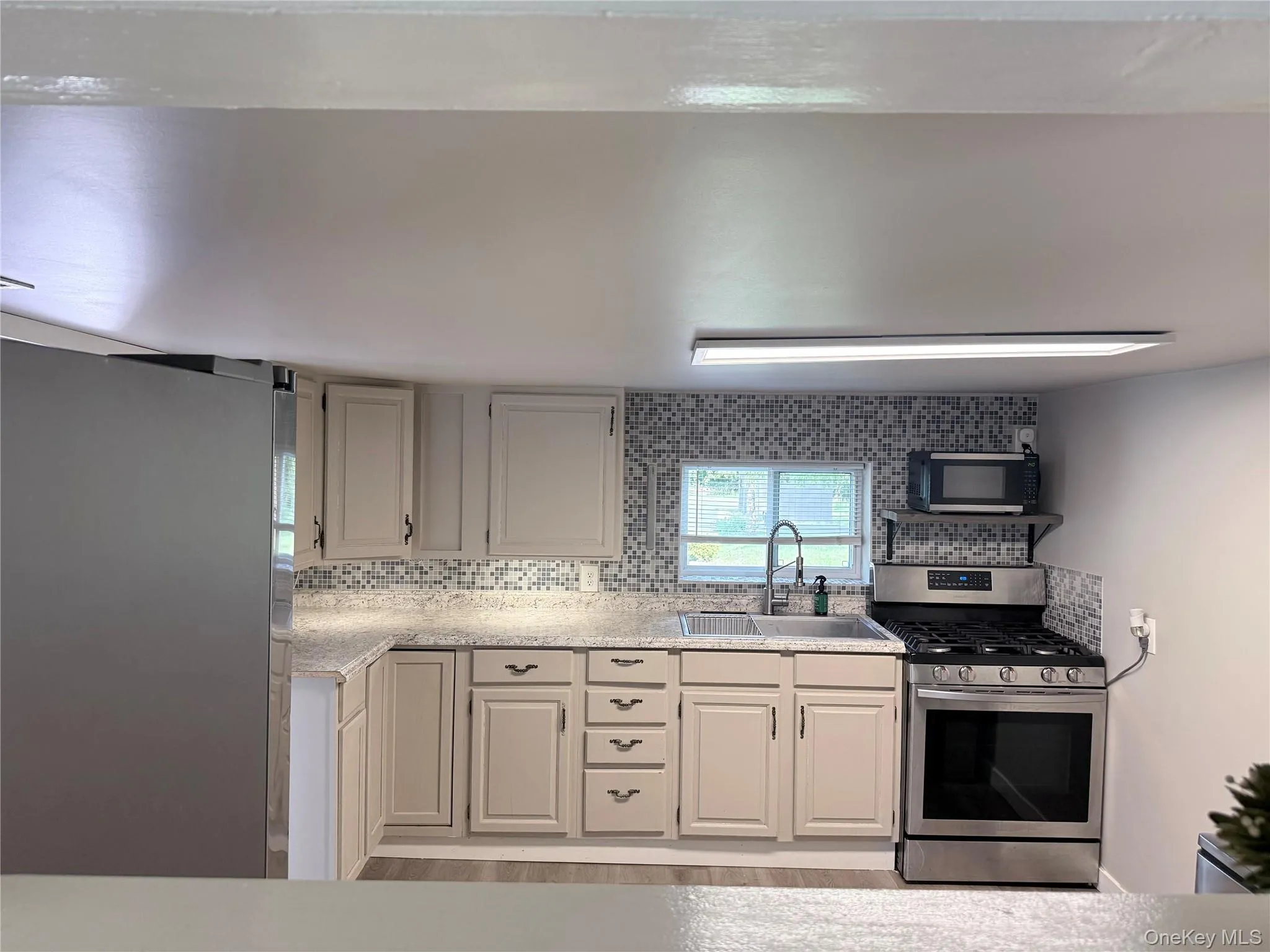 Kitchen featuring light-toned cabinetry, a mosaic tile backsplash, and wood-finish flooring Kitchen featuring light-toned cabinetry, a mosaic tile backsplash, and wood-finish flooring