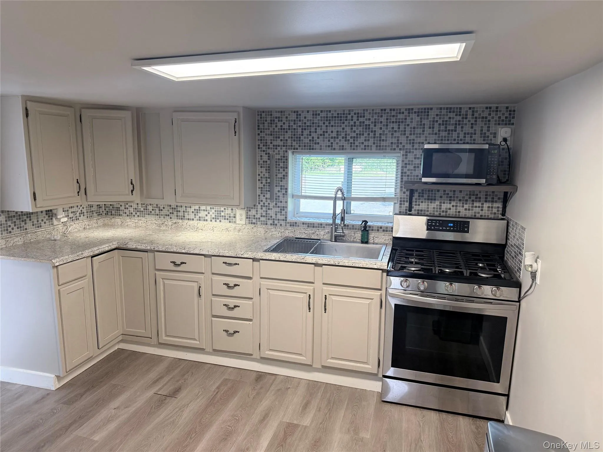Kitchen featuring granite-style countertops, mosaic tile backsplash, stainless steel gas range, and wood-finish flooring Kitchen featuring granite-style countertops, mosaic tile backsplash, stainless steel gas range, and wood-finish flooring