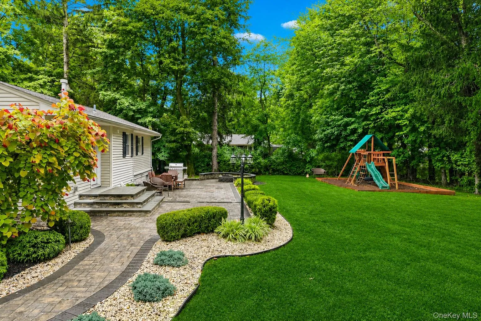 View of backyard with pavered paths, patio with fire pit, and playset View of backyard with pavered paths, patio with fire pit, and playset