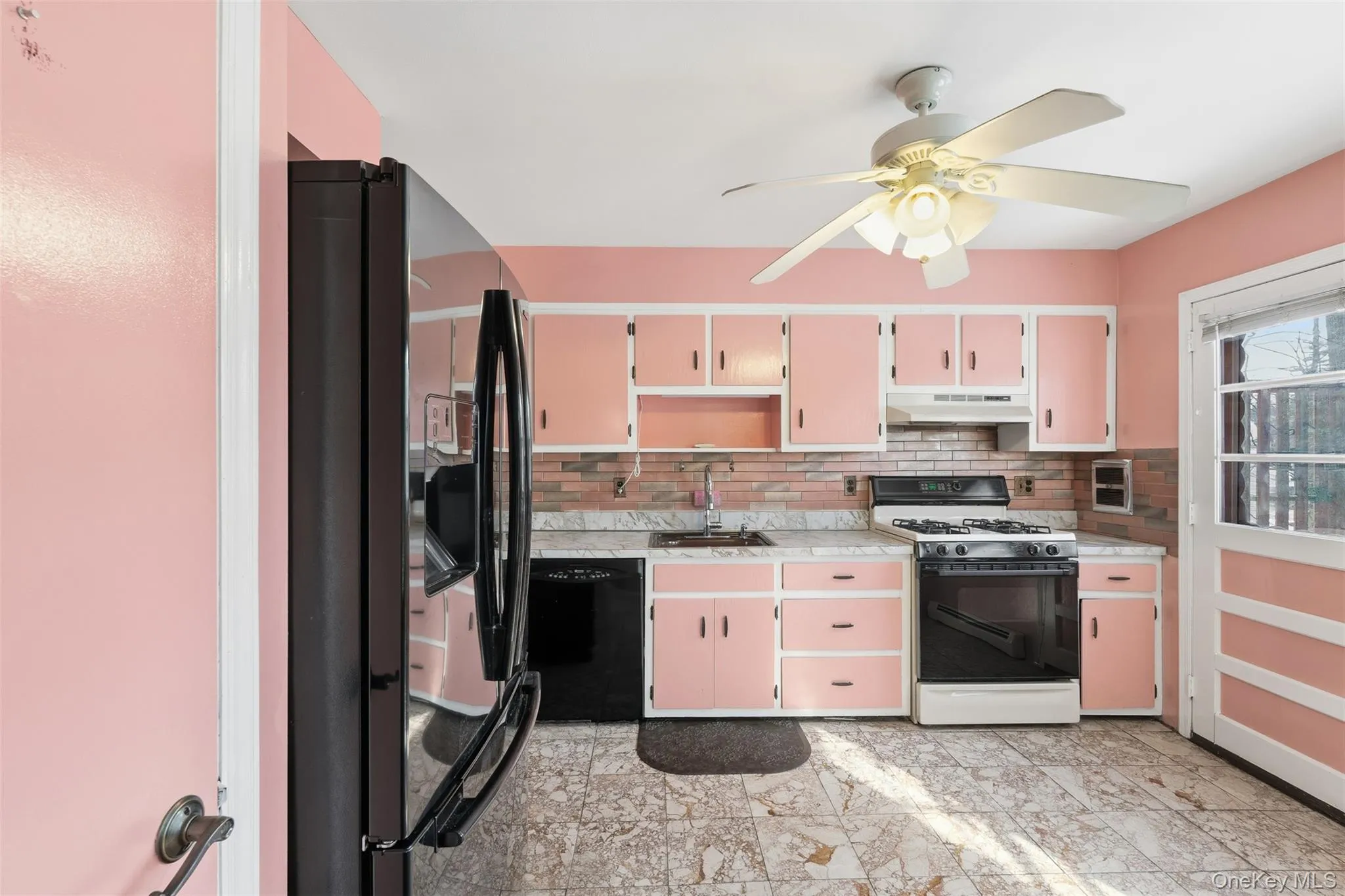 Kitchen featuring pink cabinetry with white trim, a black refrigerator, a black gas range, and a ceiling fan with integrated lighting Kitchen featuring pink cabinetry with white trim, a black refrigerator, a black gas range, and a ceiling fan with integrated lighting