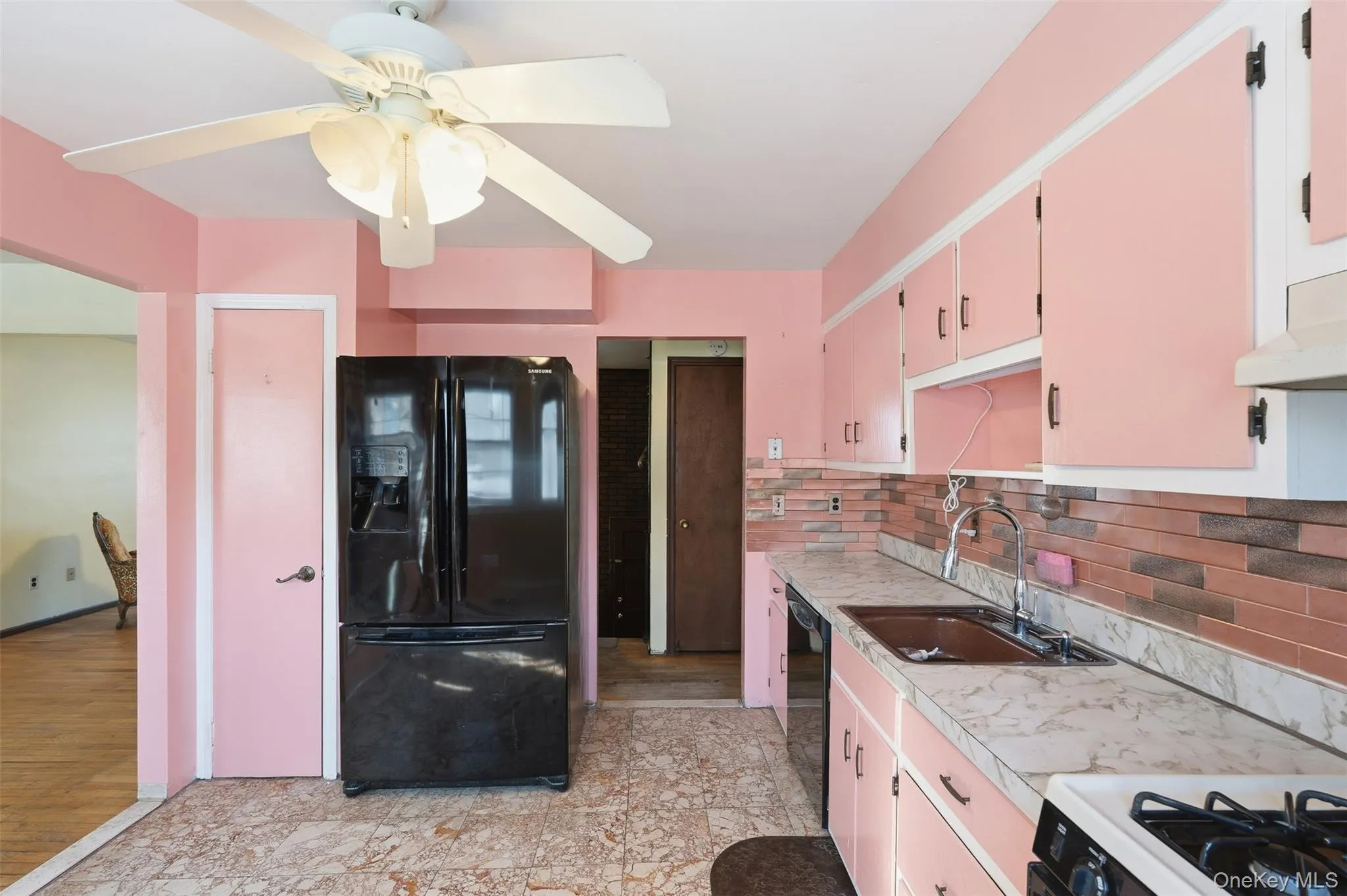 Kitchen featuring a ceiling fan, black French door refrigerator, brown tiled backsplash, double basin sink with gooseneck faucet, and light-toned countertops Kitchen featuring a ceiling fan, black French door refrigerator, brown tiled backsplash, double basin sink with gooseneck faucet, and light-toned countertops