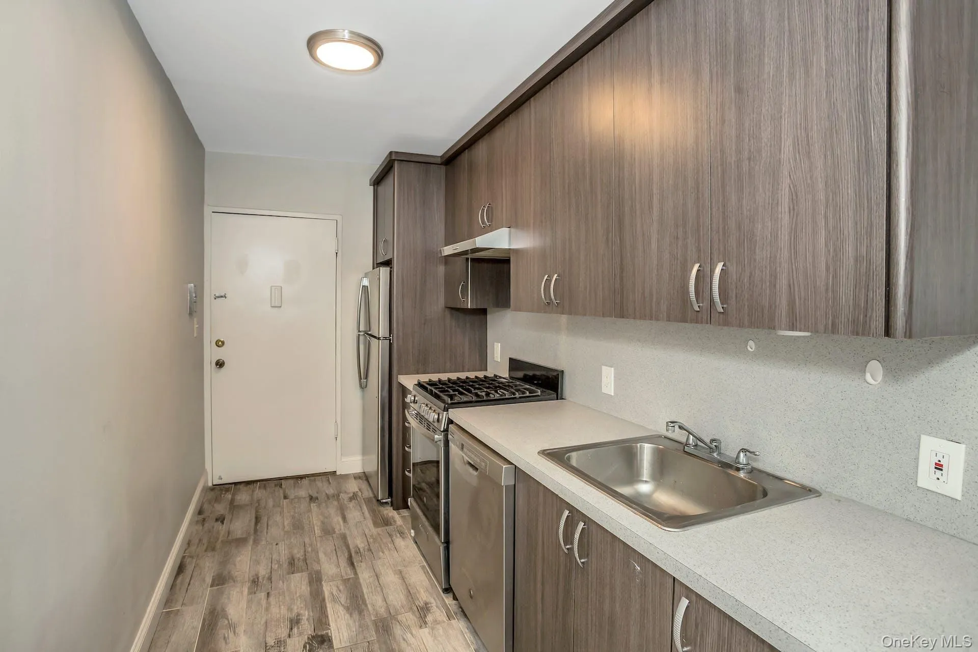 Kitchen with a sink, light countertops, appliances with stainless steel finishes, under cabinet range hood, and light wood-style flooring Kitchen with a sink, light countertops, appliances with stainless steel finishes, under cabinet range hood, and light wood-style flooring