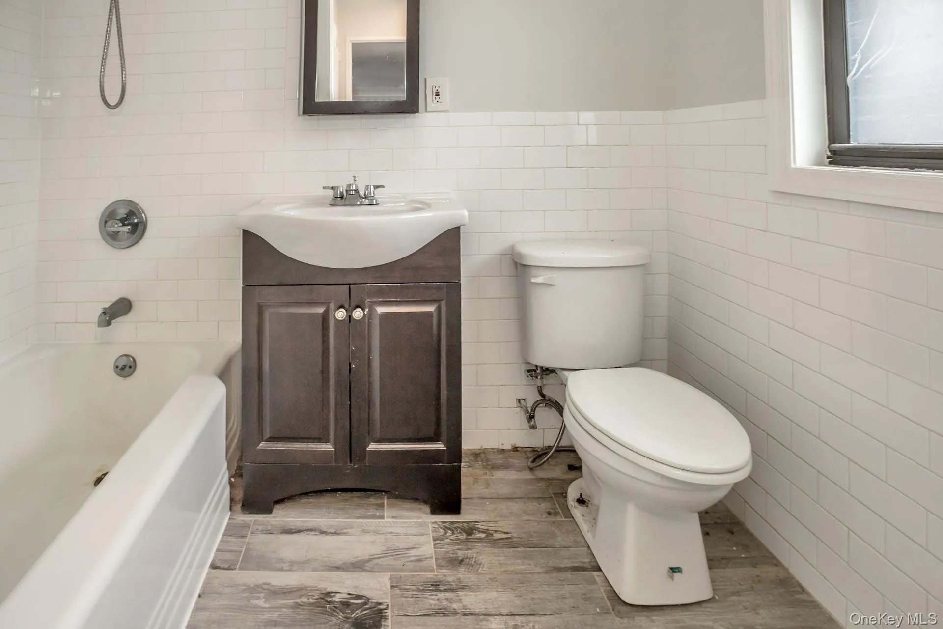 Full bathroom featuring tile walls, toilet, bathtub / shower combination, vanity, and wood finished floors Full bathroom featuring tile walls, toilet, bathtub / shower combination, vanity, and wood finished floors