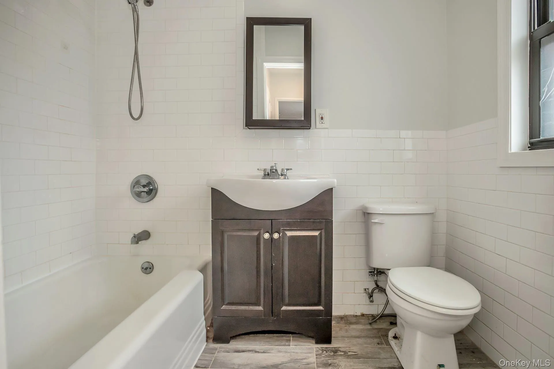 Bathroom featuring bathing tub / shower combination, vanity, toilet, wood finished floors, and tile walls Bathroom featuring bathing tub / shower combination, vanity, toilet, wood finished floors, and tile walls