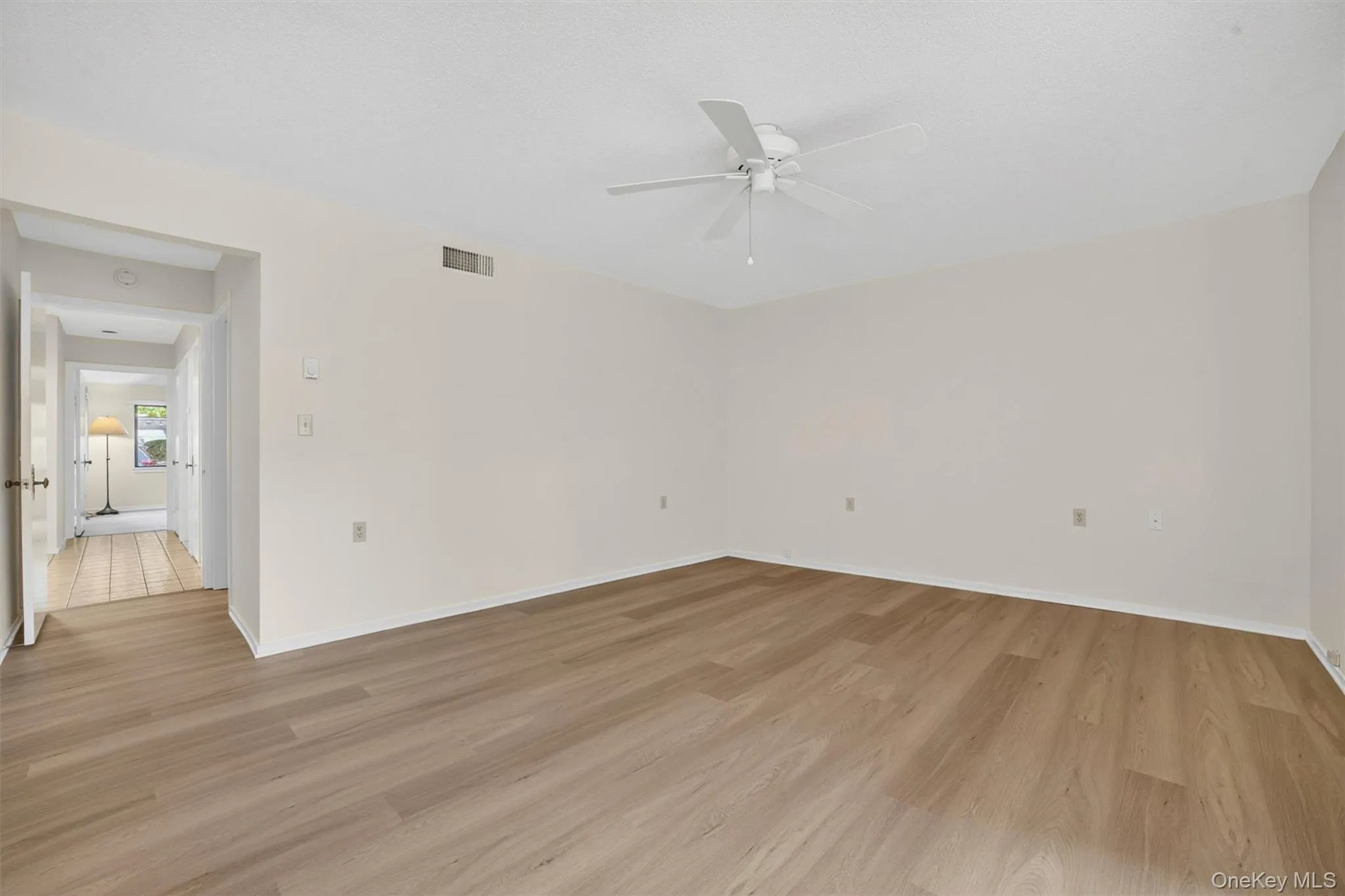 Spacious room featuring wood-finish flooring, a white ceiling fan, and neutral wall tones Spacious room featuring wood-finish flooring, a white ceiling fan, and neutral wall tones