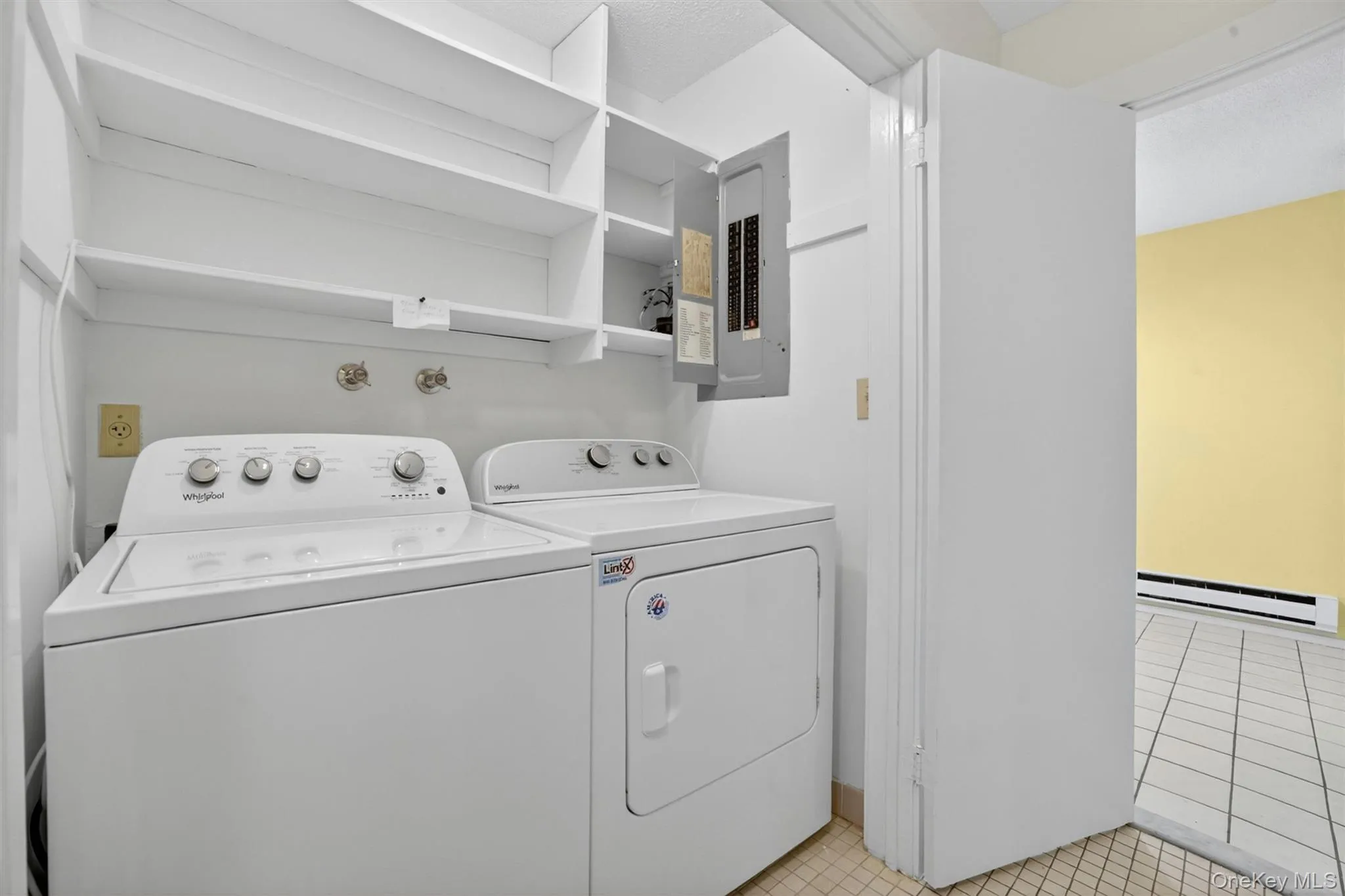 Dedicated laundry area featuring white shelving, a utility outlet, and tile flooring Dedicated laundry area featuring white shelving, a utility outlet, and tile flooring