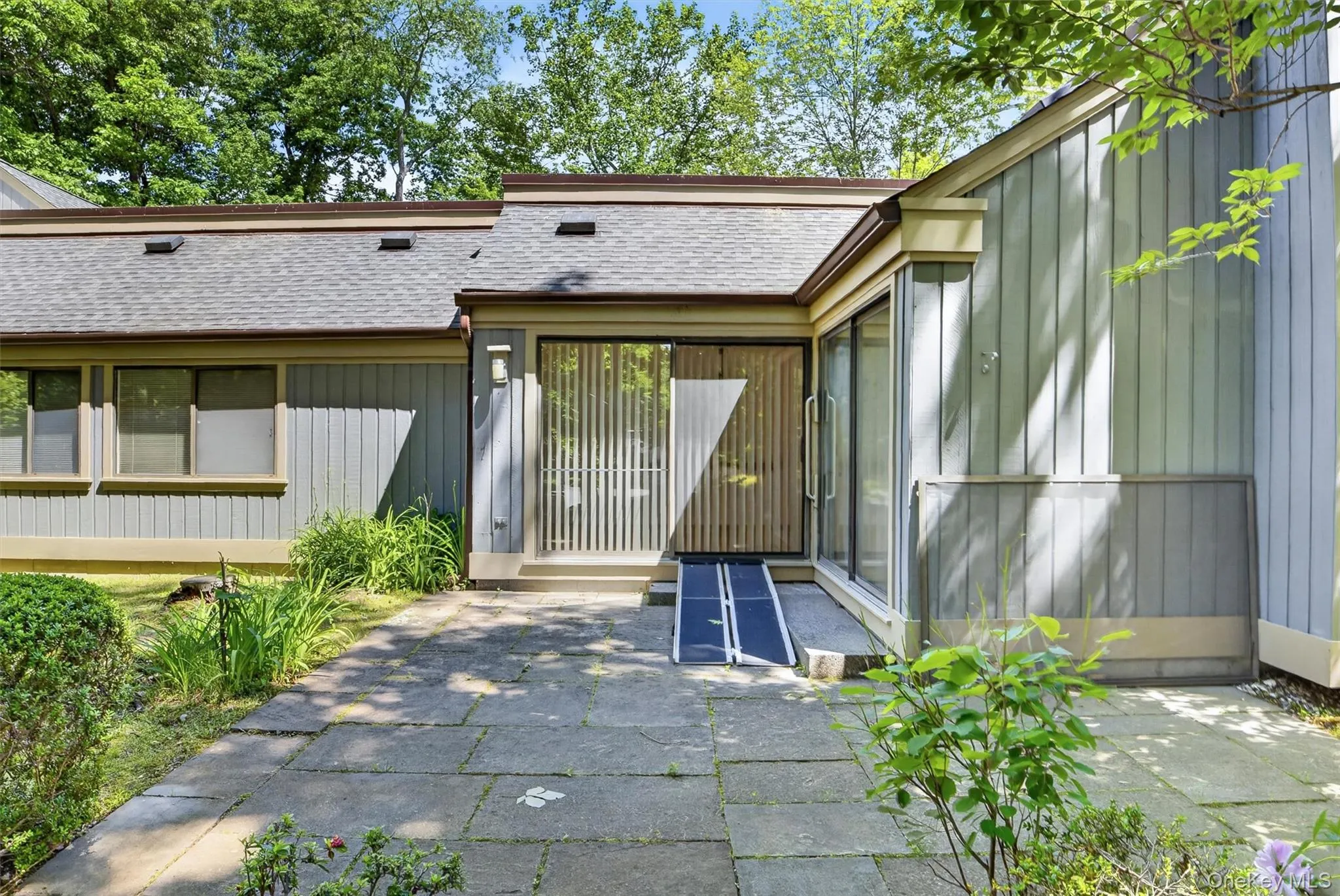 Front entrance featuring a stone paver pathway, large sliding glass doors, vertical blinds, a wheelchair ramp, and board-and-batten siding Front entrance featuring a stone paver pathway, large sliding glass doors, vertical blinds, a wheelchair ramp, and board-and-batten siding