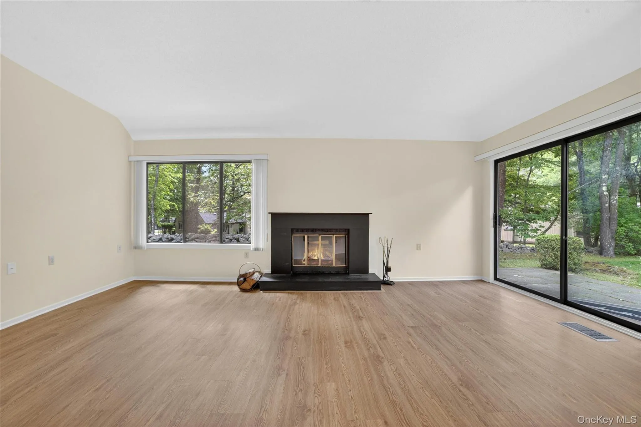 Spacious living area featuring wood-finish flooring, a fireplace with a dark surround, and large sliding glass doors providing access to the outdoors Spacious living area featuring wood-finish flooring, a fireplace with a dark surround, and large sliding glass doors providing access to the outdoors