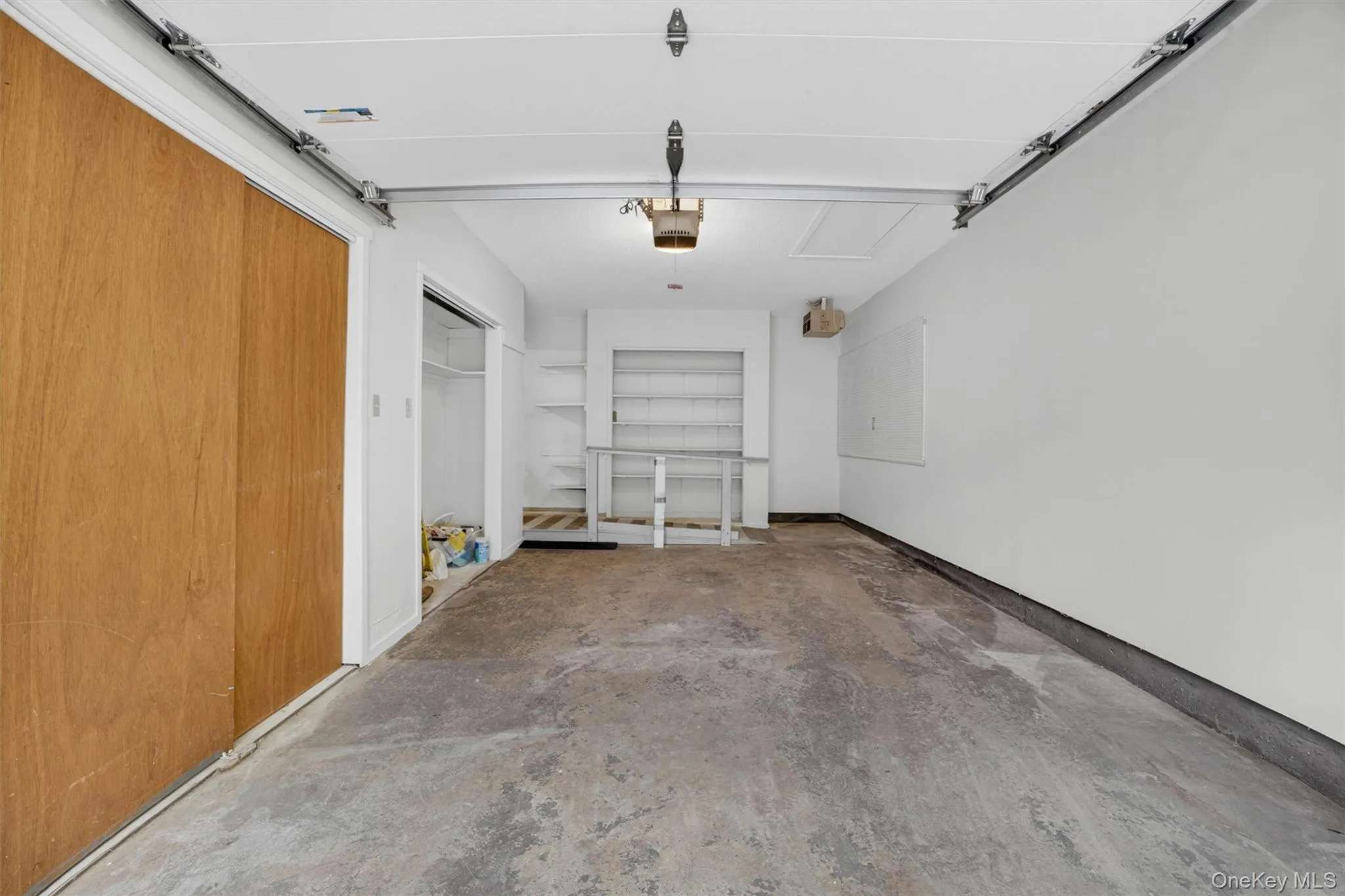 Spacious garage featuring a concrete floor, bright white walls, built-in shelving, a built-in workbench, and a large wood-finish sliding door Spacious garage featuring a concrete floor, bright white walls, built-in shelving, a built-in workbench, and a large wood-finish sliding door